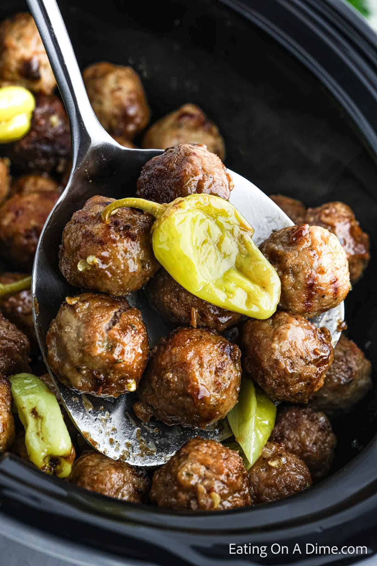 Cooked meatballs on a serving spoons with a pepper on top. In the background is a crock pot full of meatballs