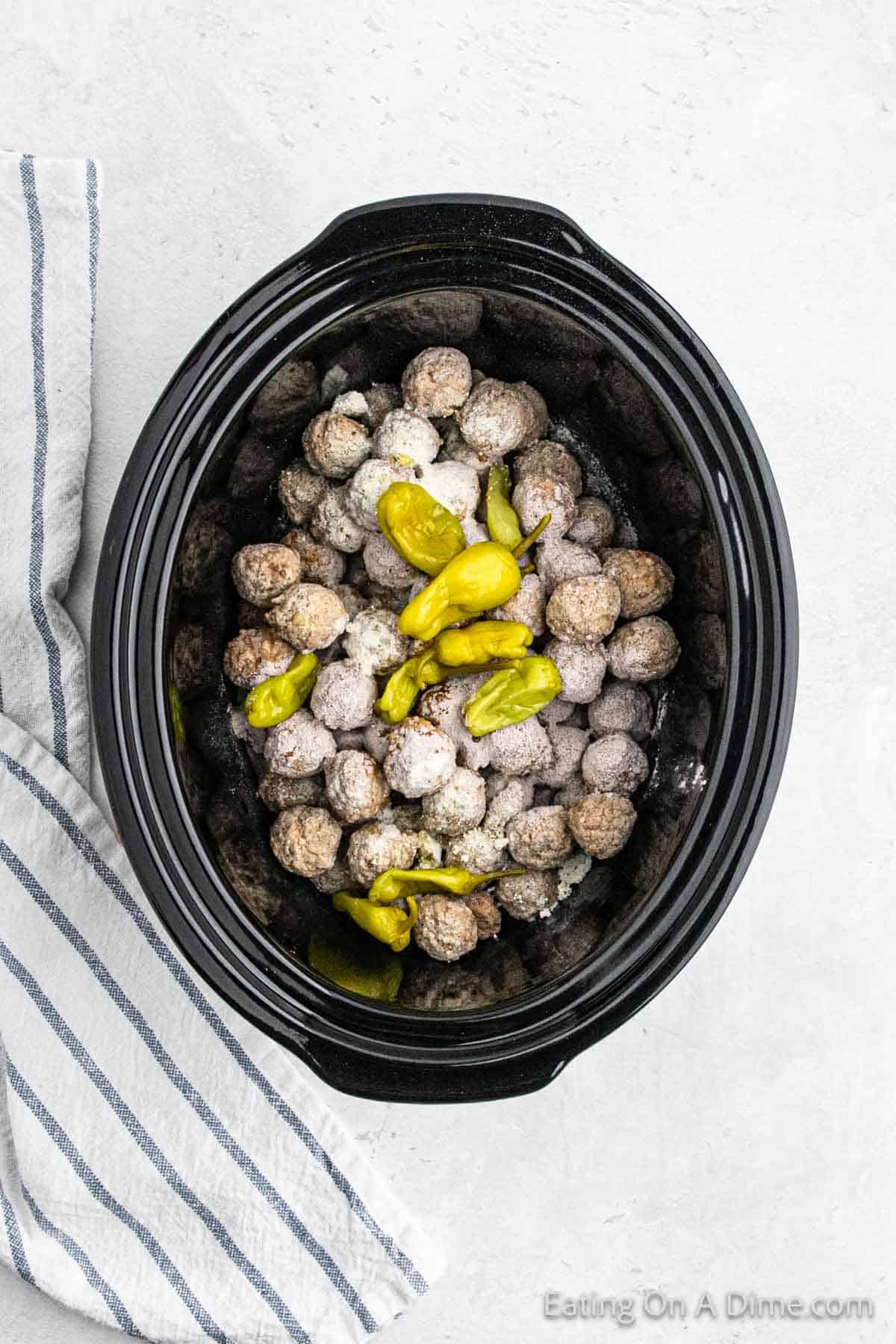 Topping the seasoned uncooked meatballs with peppers in the slow cooker