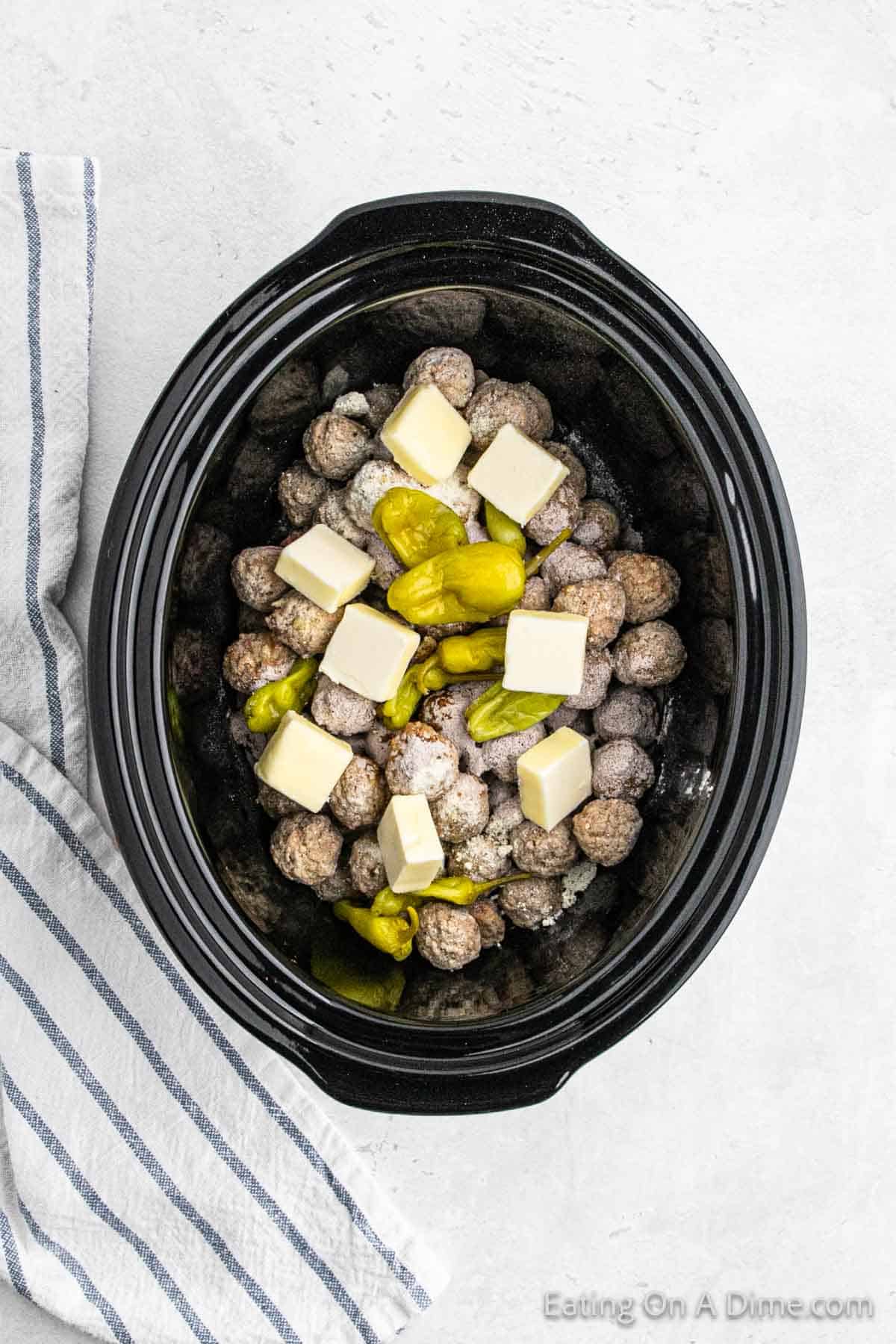 Topping the seasoned meatballs with slice butter and peppers in the slow cooker