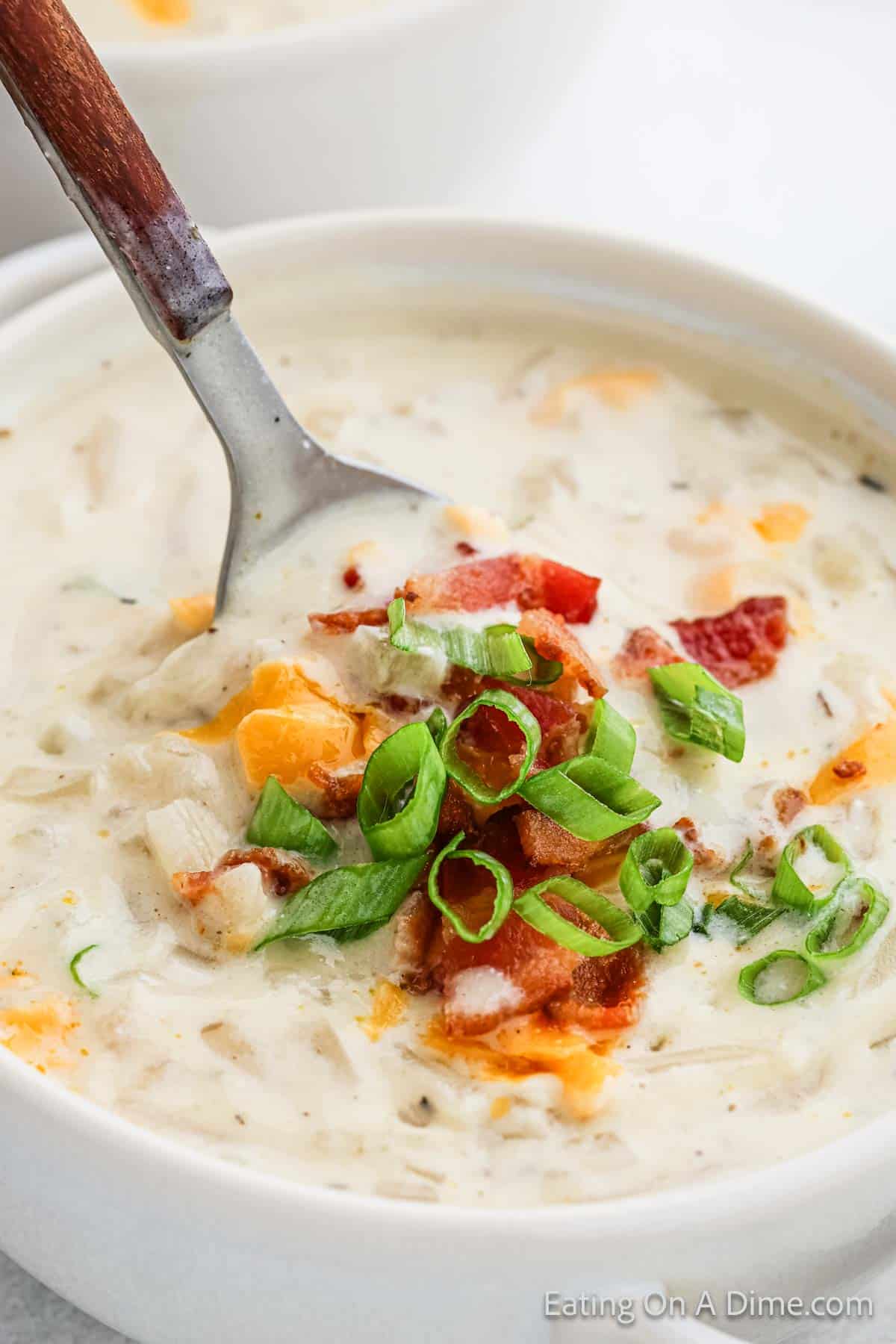 Potato Soup in a white bowl topped with melted cheese, green onions and chopped bacon