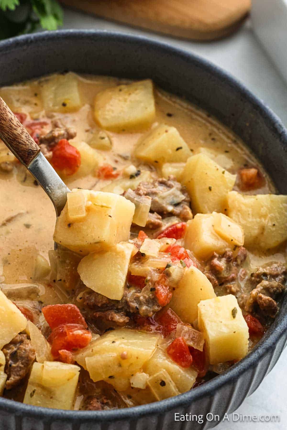 Hamburger and potato soup in a bowl with a bite on a spoon