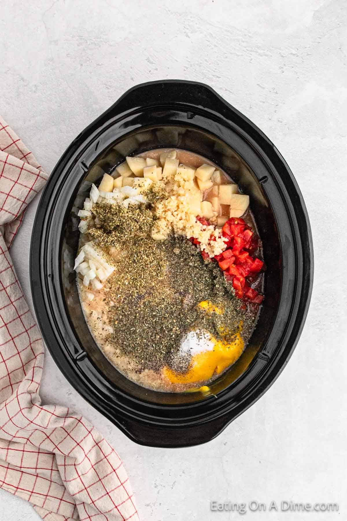 Adding the diced potatoes, seasoning, cheese soup, diced tomatoes and onions in the slow cooker