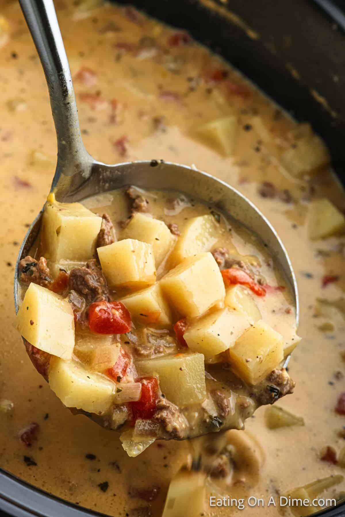 Potato and hamburger soup in the slow cooker with a serving on the ladle. 