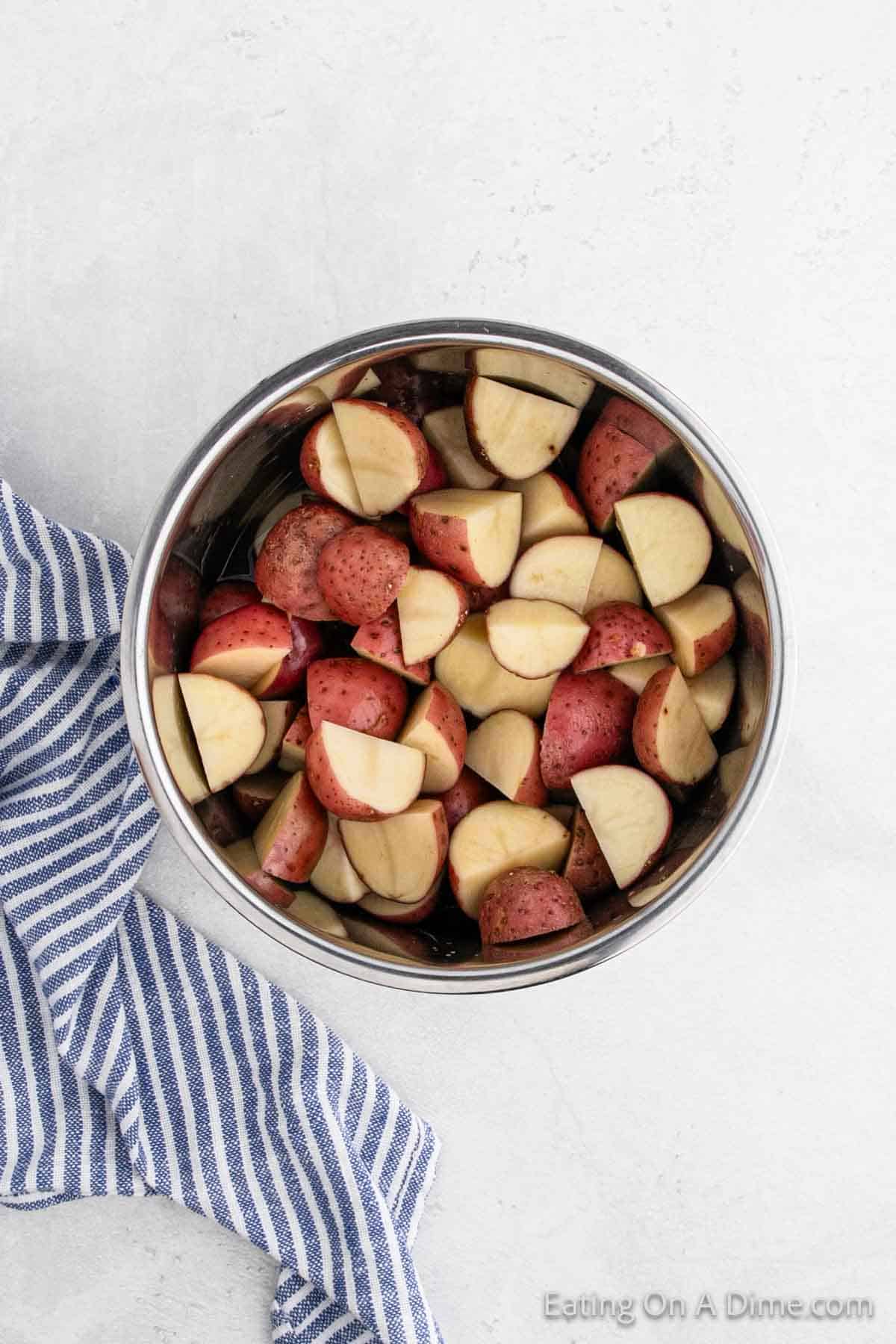 A bowl of chopped red potatoes rests on a gray surface beside a blue and white striped cloth, perfect for transforming into creamy mashed red potatoes.