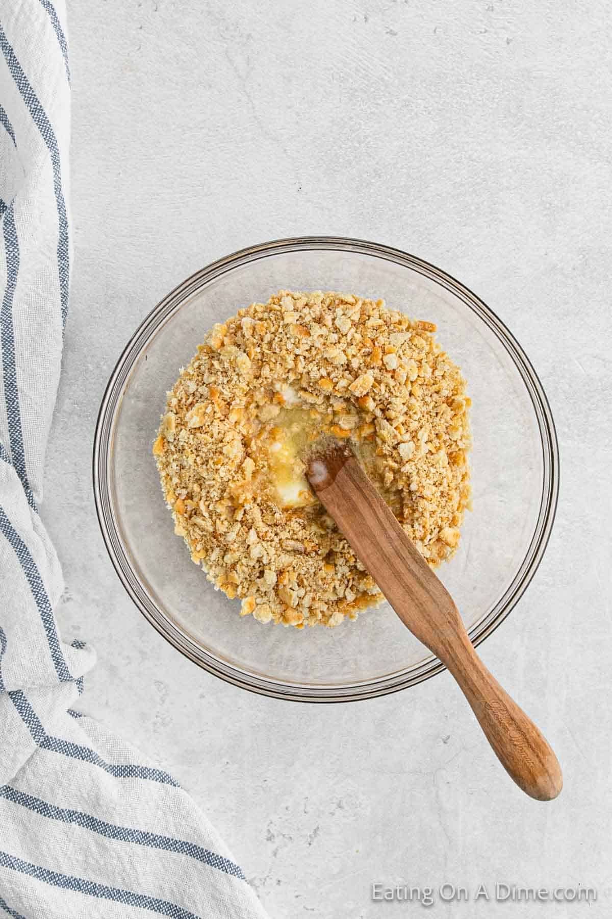 Crushed Ritz Crackers in a melted butter in a bowl with a wooden spoon