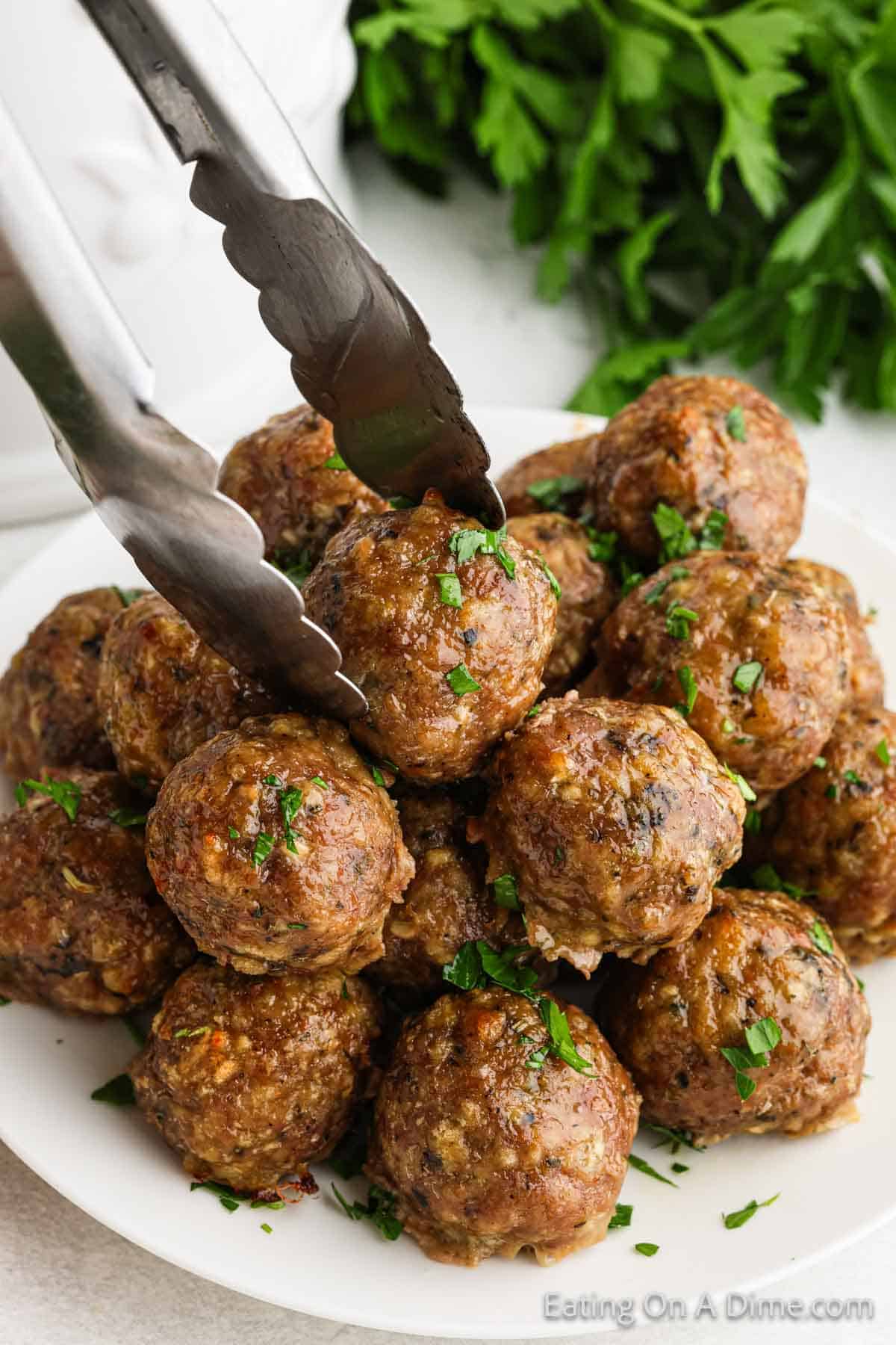 Turkey Meatballs stacked on a plate with a silver tongs on one of them