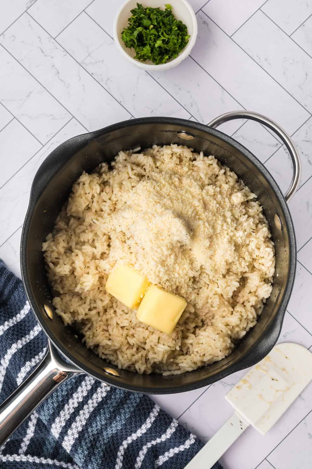 Cooked white rice in a sauce pan topped with butter slices and parmesan cheese