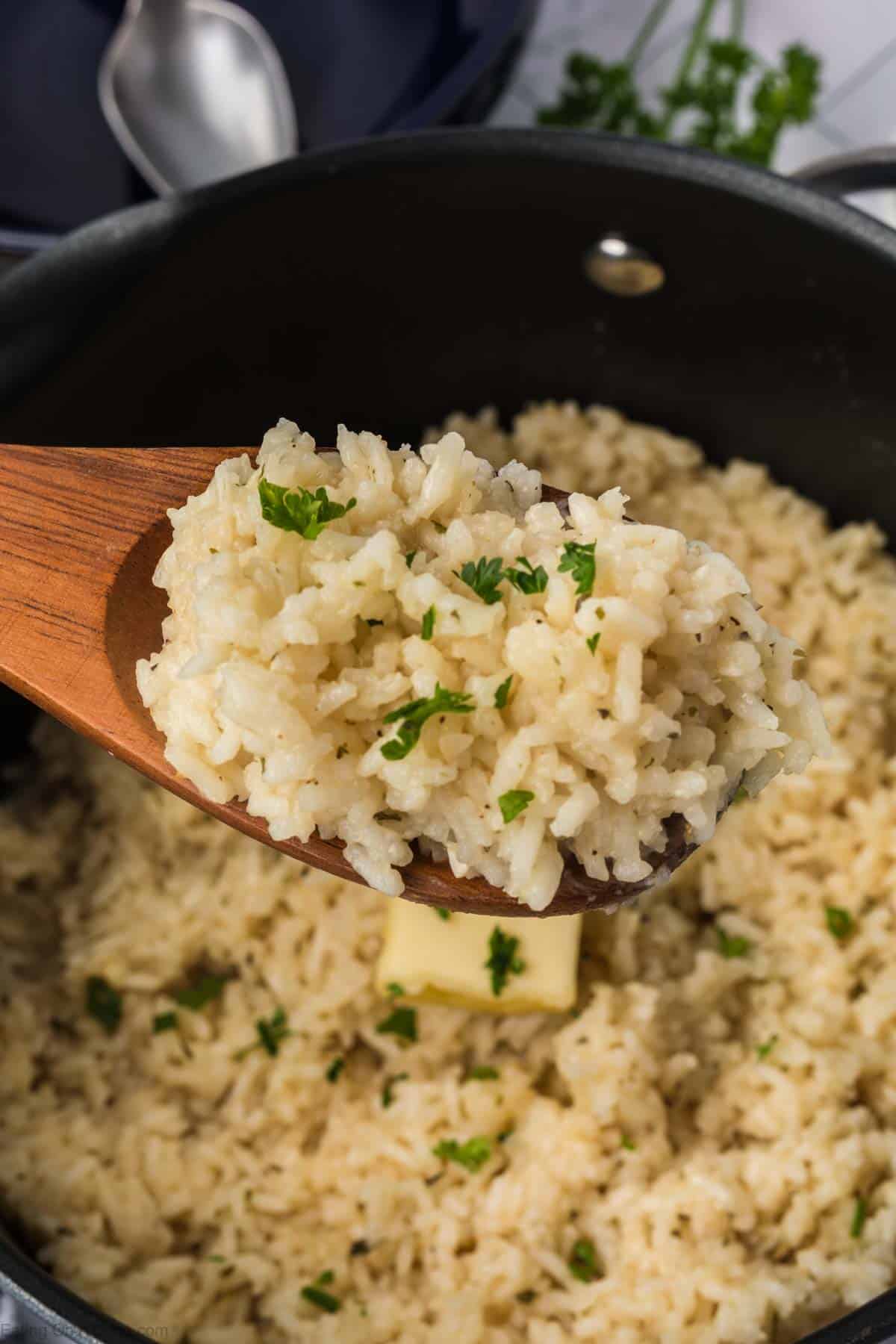 White rice in a large saucepan with a serving on a wooden spoon