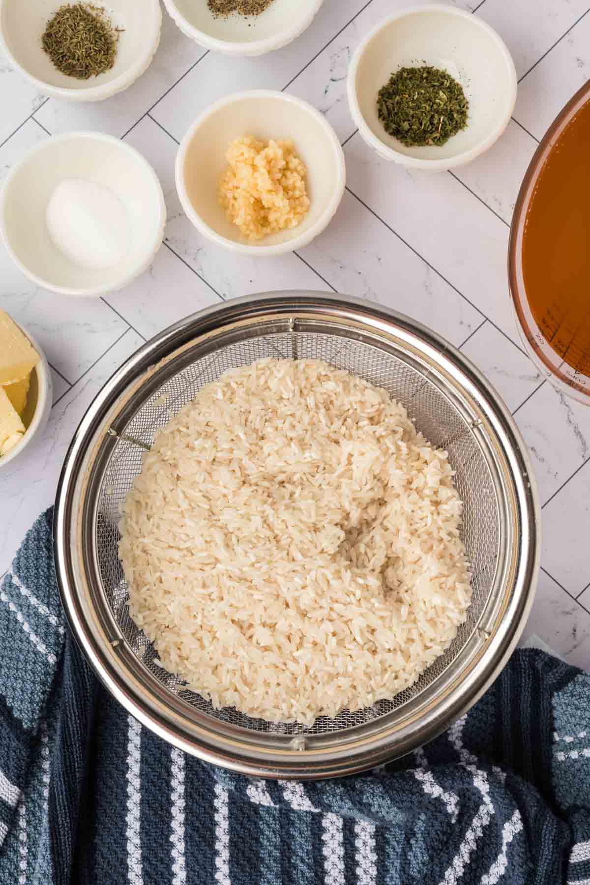 Rinsing white rice in a colander with small bowls of seasoning on the side