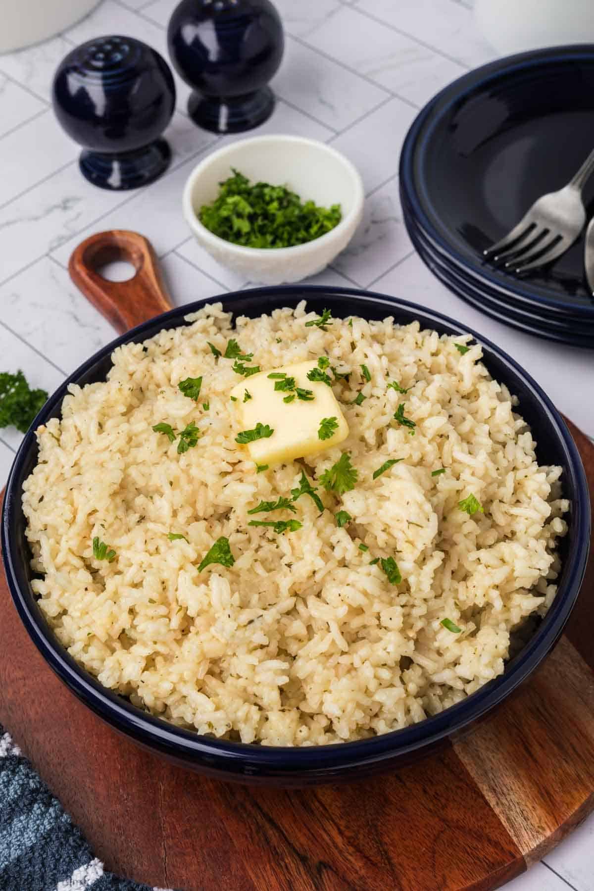 Cooked white Rice topped with butter slice and chopped parsley in a blue dish