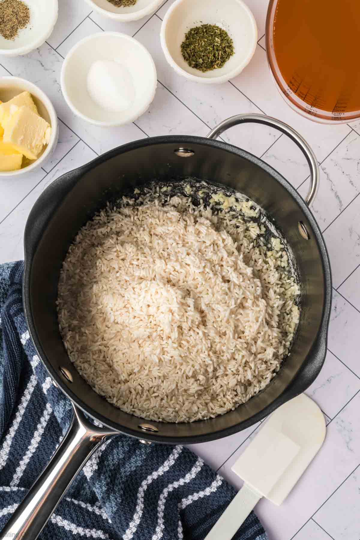 Adding white rice with the melted butter in a cast iron skillet with small bowls of seasoning