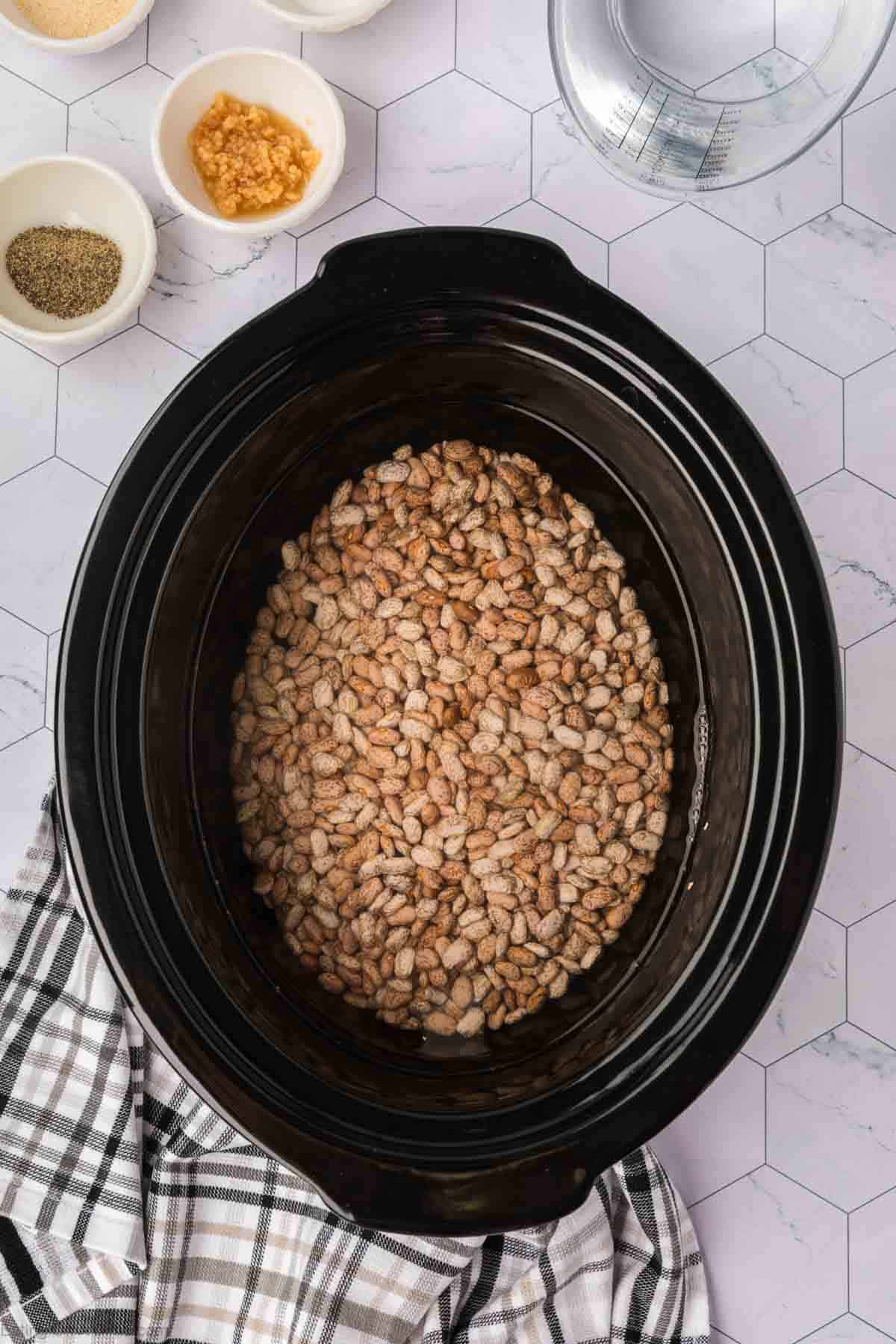 Brown beans in the slow cooker with small bowls of seasoning on the side