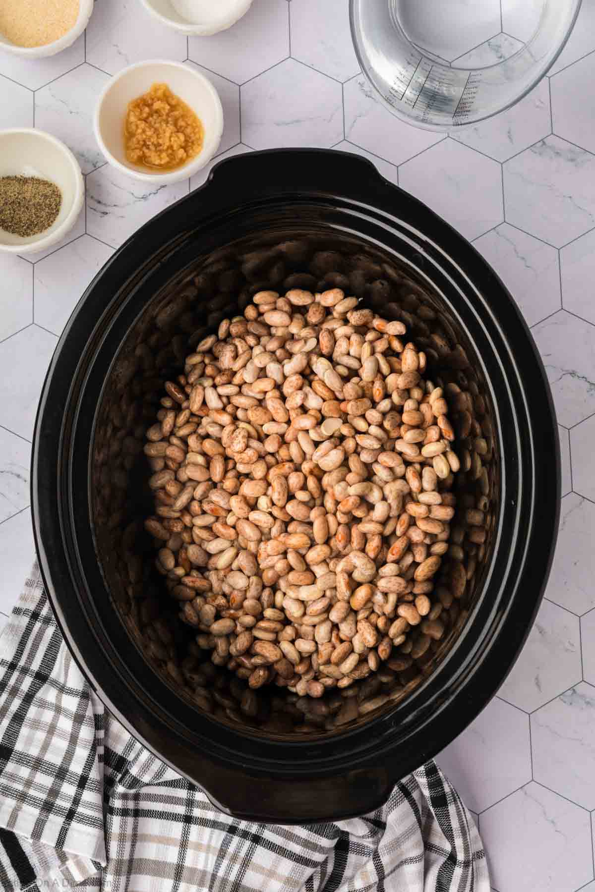 Drained beans in the slow cooker with small bowls of seasoning on the side