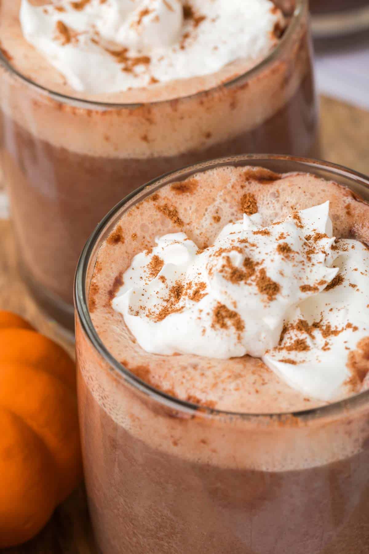 Pumpkin Spice Hot Chocolate in a clear mug topped with whipped cream and ground cinnamon