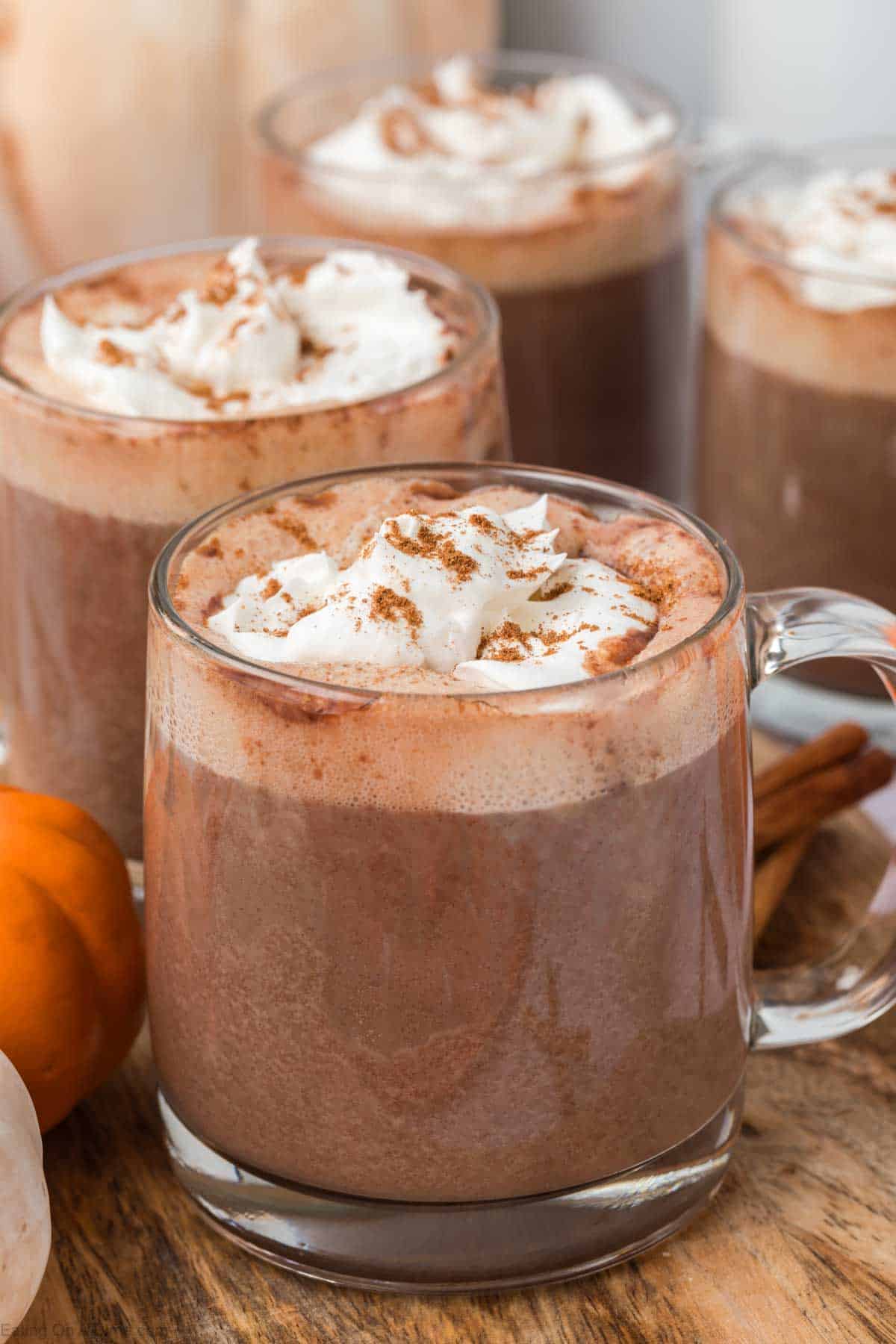 Pumpkin Spice Hot Chocolate in clear mugs topped with whipped cream and ground cinnamon