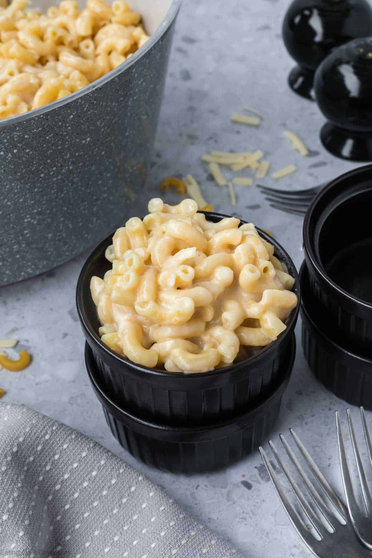 White Cheddar Mac and Cheese in a small black bowl with a large pot of mac and cheese in the background