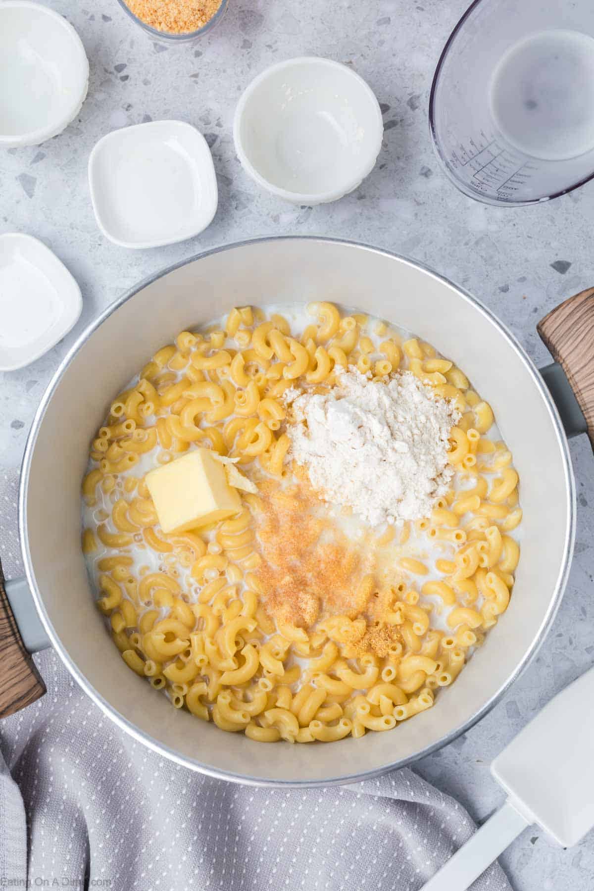 Adding milk, flour, butter and seasoning to large pot of cooked macaroni noodles