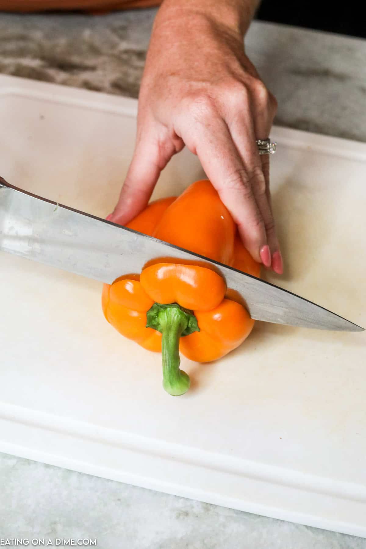 Cutting the top of the orange bell pepper with a knife on a cutting board