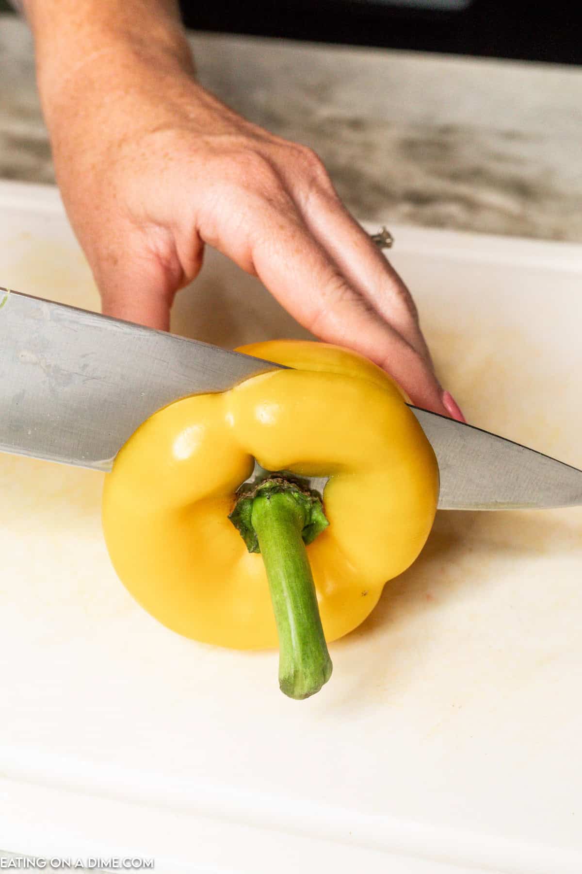 Cutting the top of a yellow bell pepper with a knife