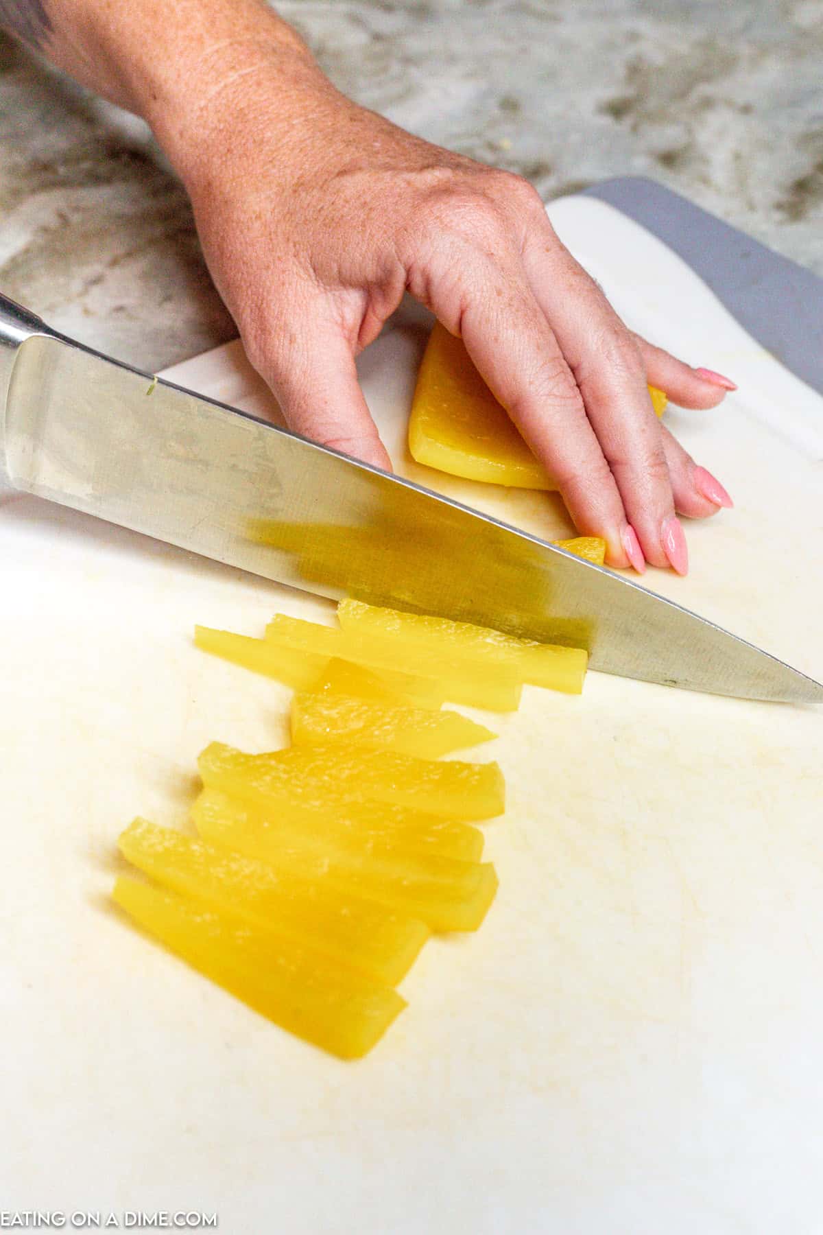 Cutting the yellow bell pepper into strips with a knife on a cutting board