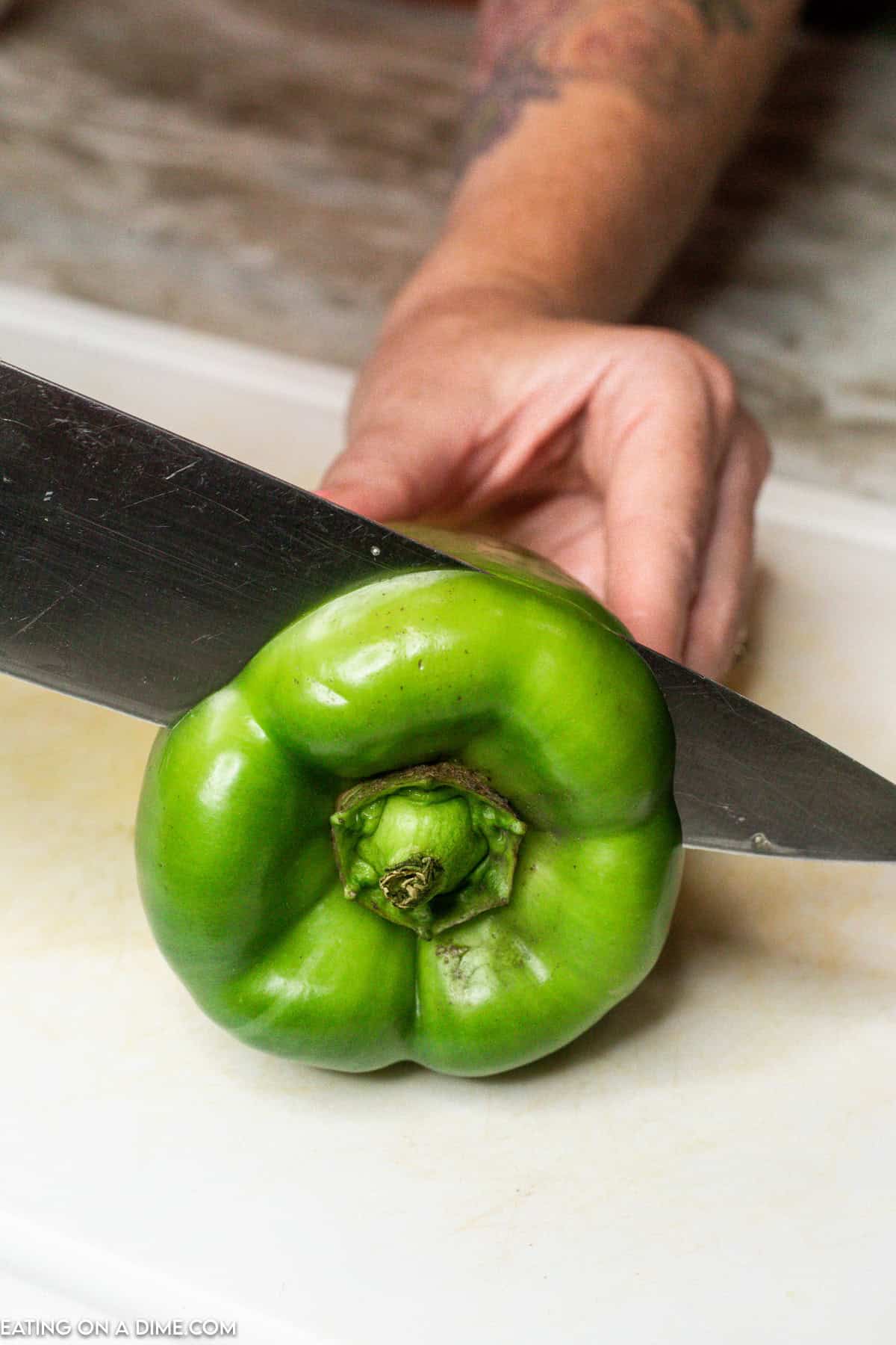 Cutting the top of a green bell pepper with a knife on a cutting board