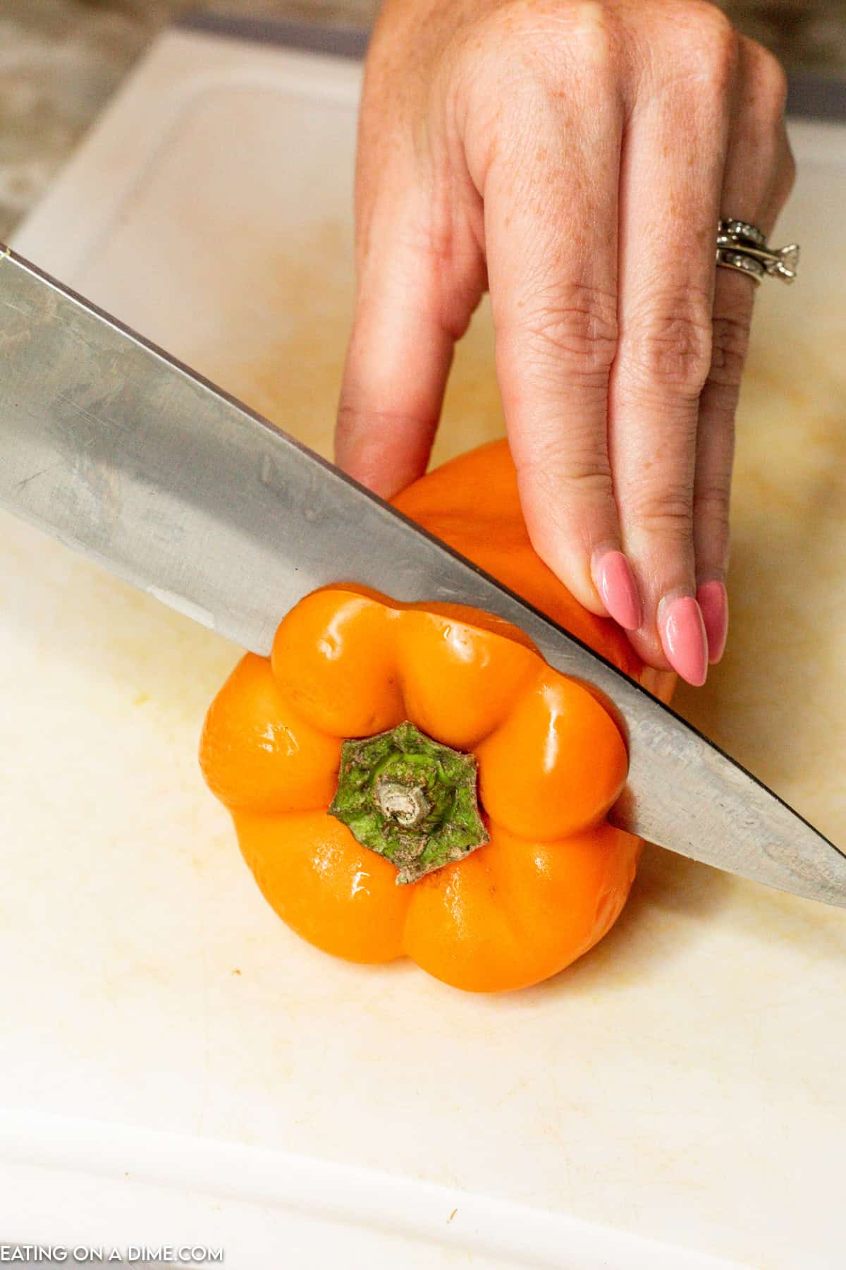 Cutting the top of the orange bell pepper with a knife