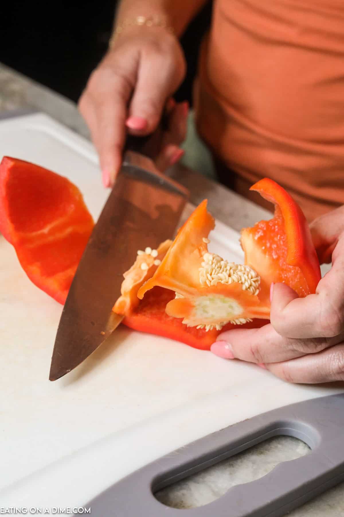 Slicing the membranes off the red bell pepper with a knife on a cutting board