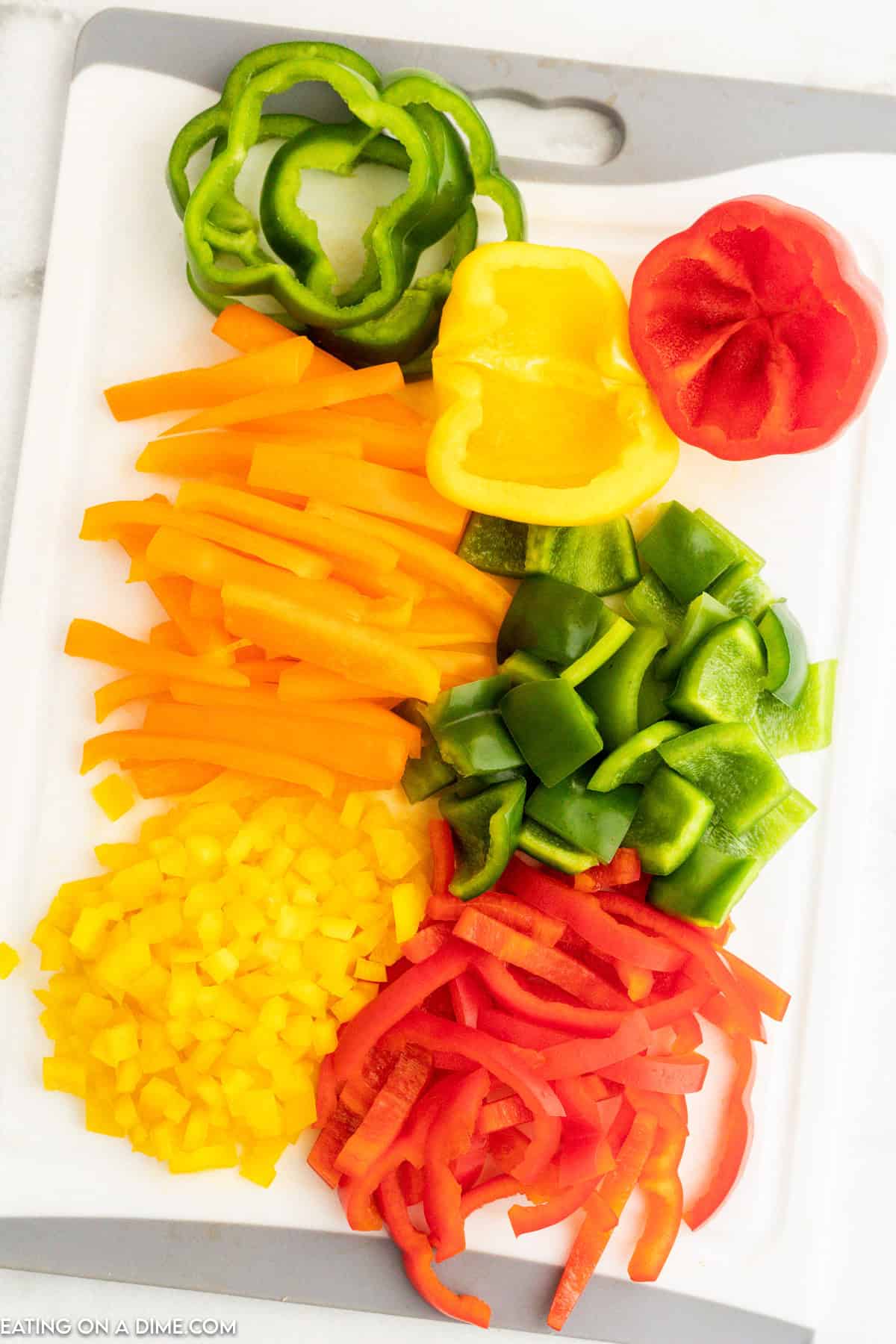 Green, orange, red, and yellow bell peppers cut into strips and bite size pieces on a cutting board