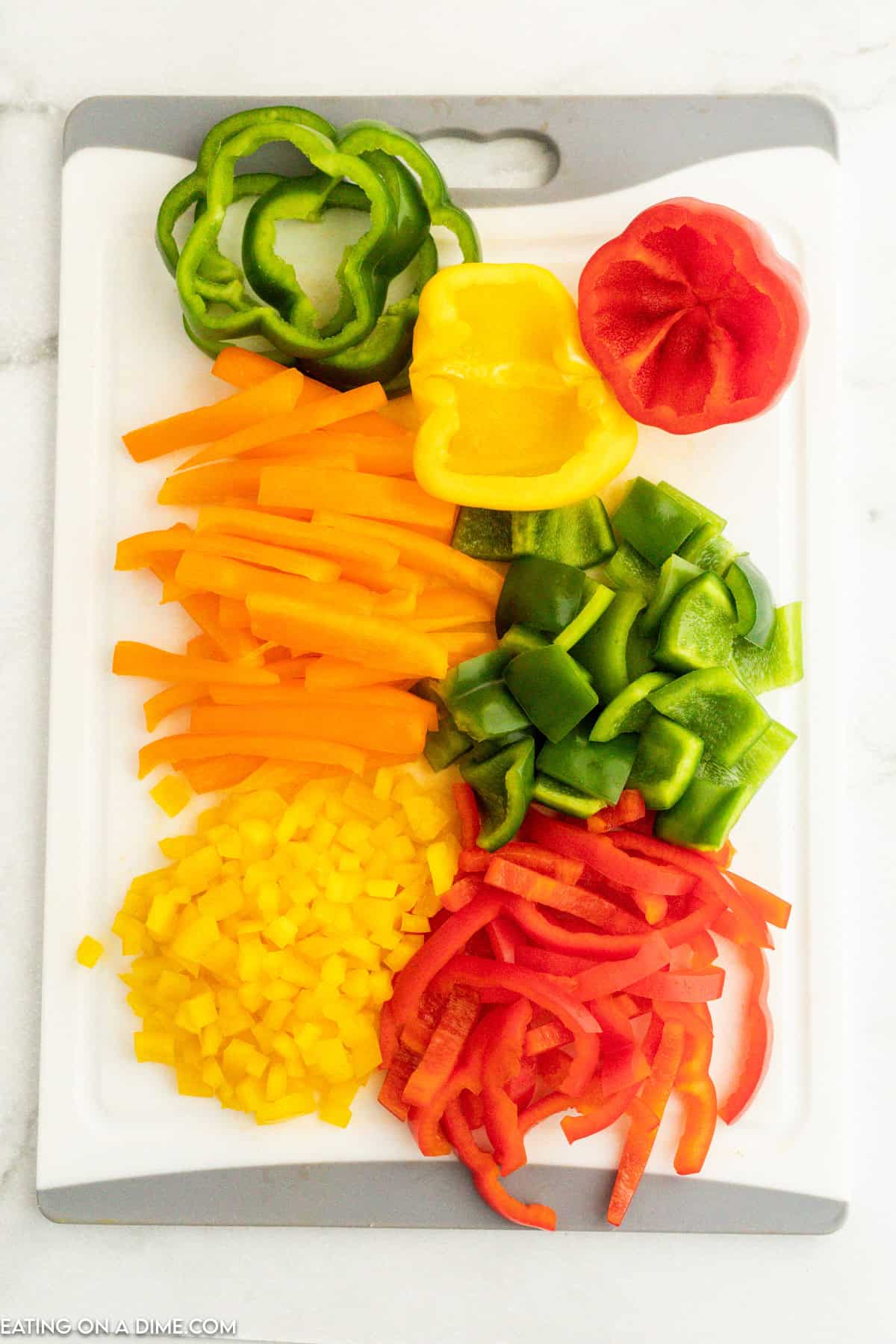 Green, orange, red, and yellow bell peppers cut into strips and bite size pieces on a cutting board