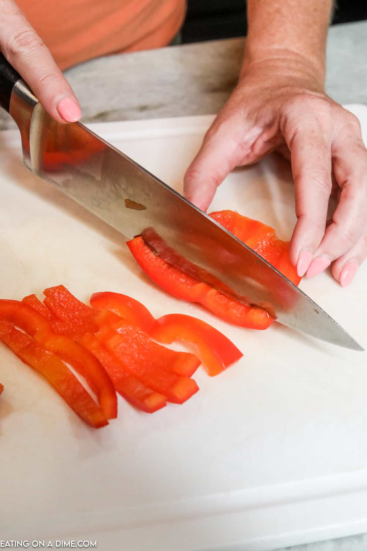 Cutting bell peppers into strips with a knife on a cutting board