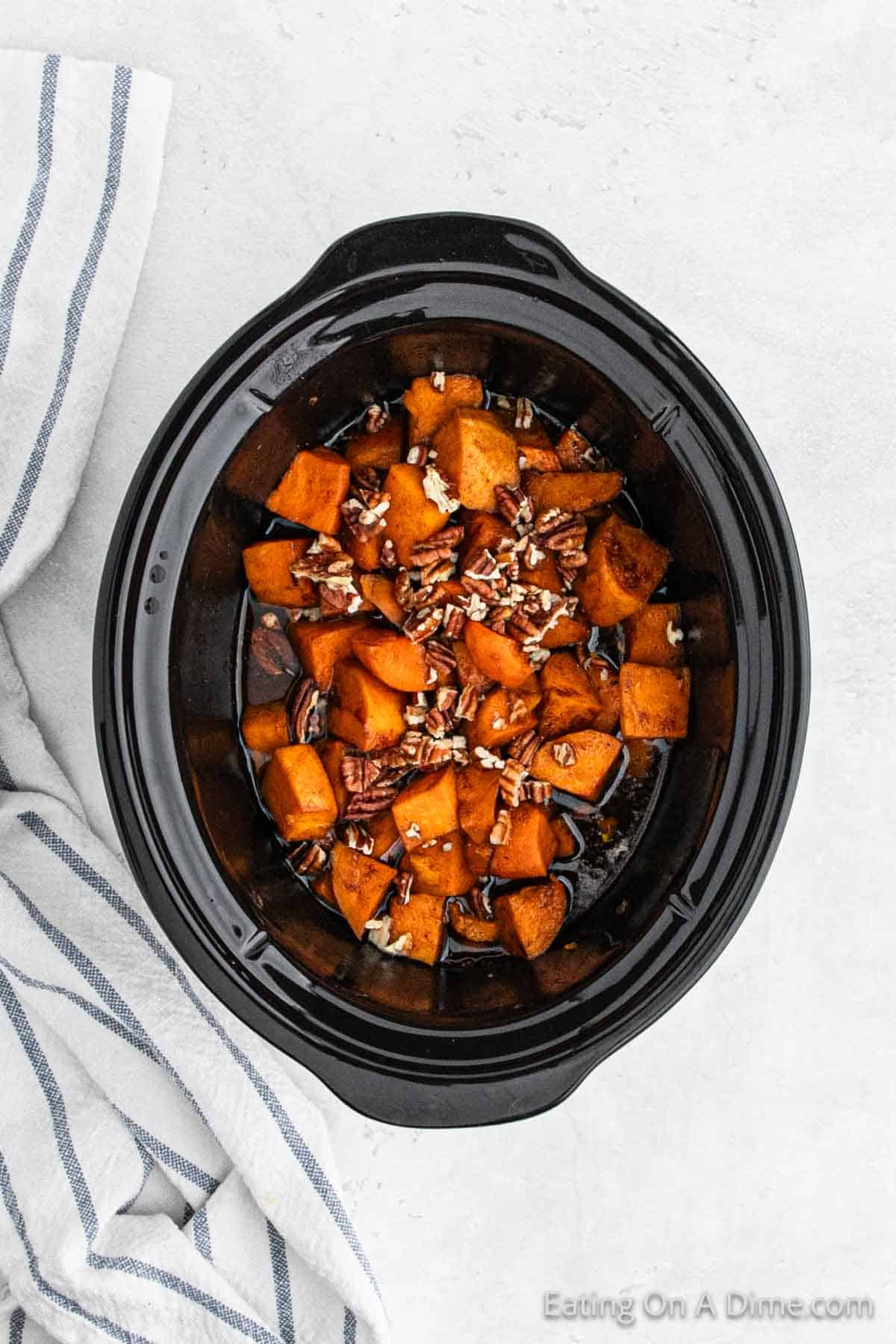 Topping the cooked candied sweet potatoes with pecans in the slow cooker