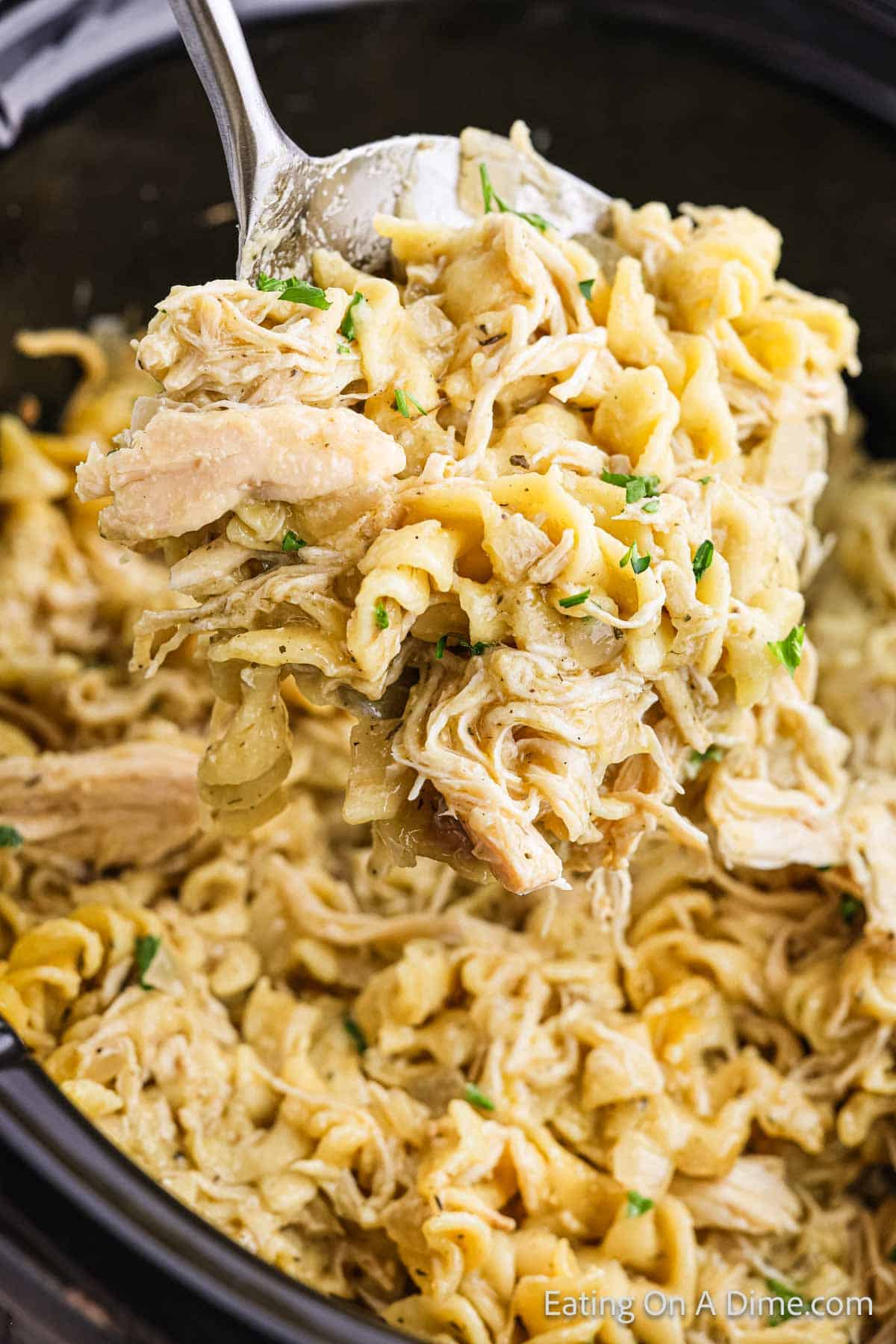 Cooked chicken and noodles in the slow cooker with a serving on a ladle