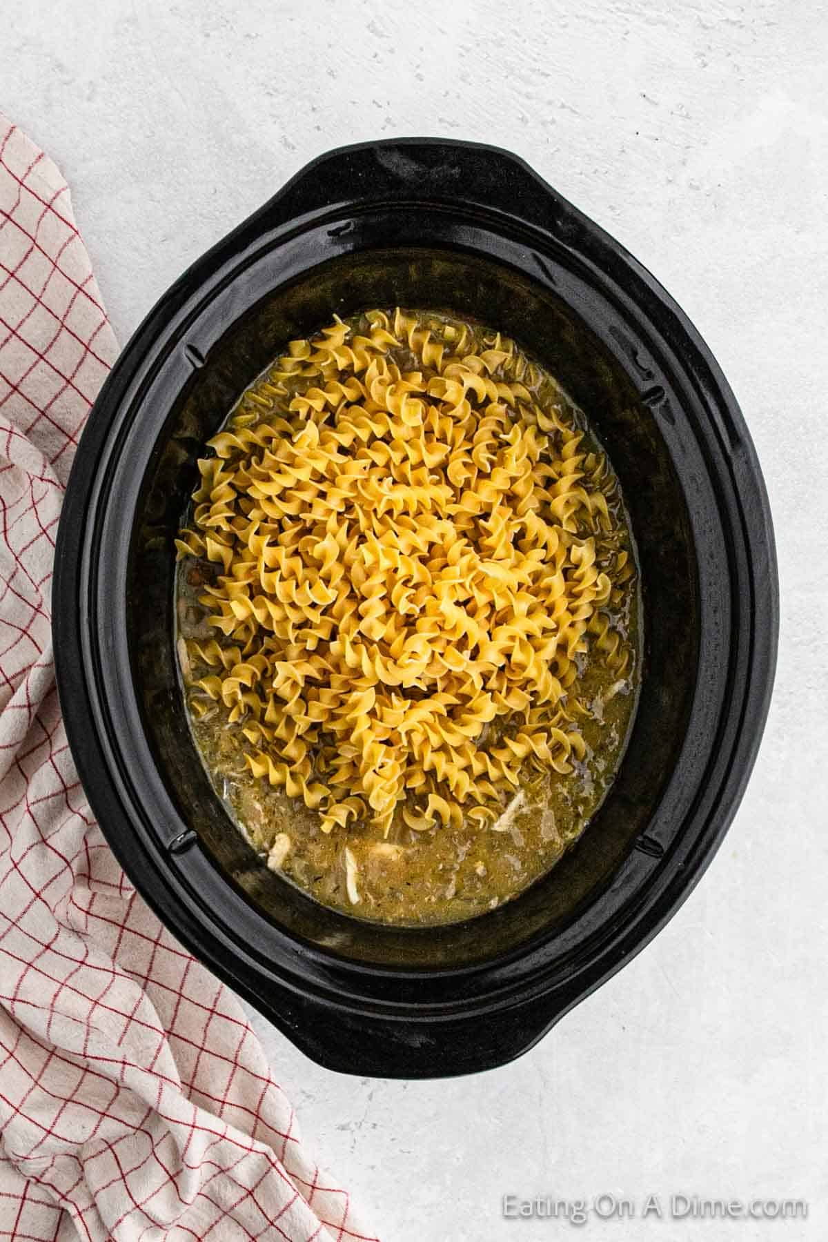 Rotini noodles added to the slow cooker with the sauce and chicken