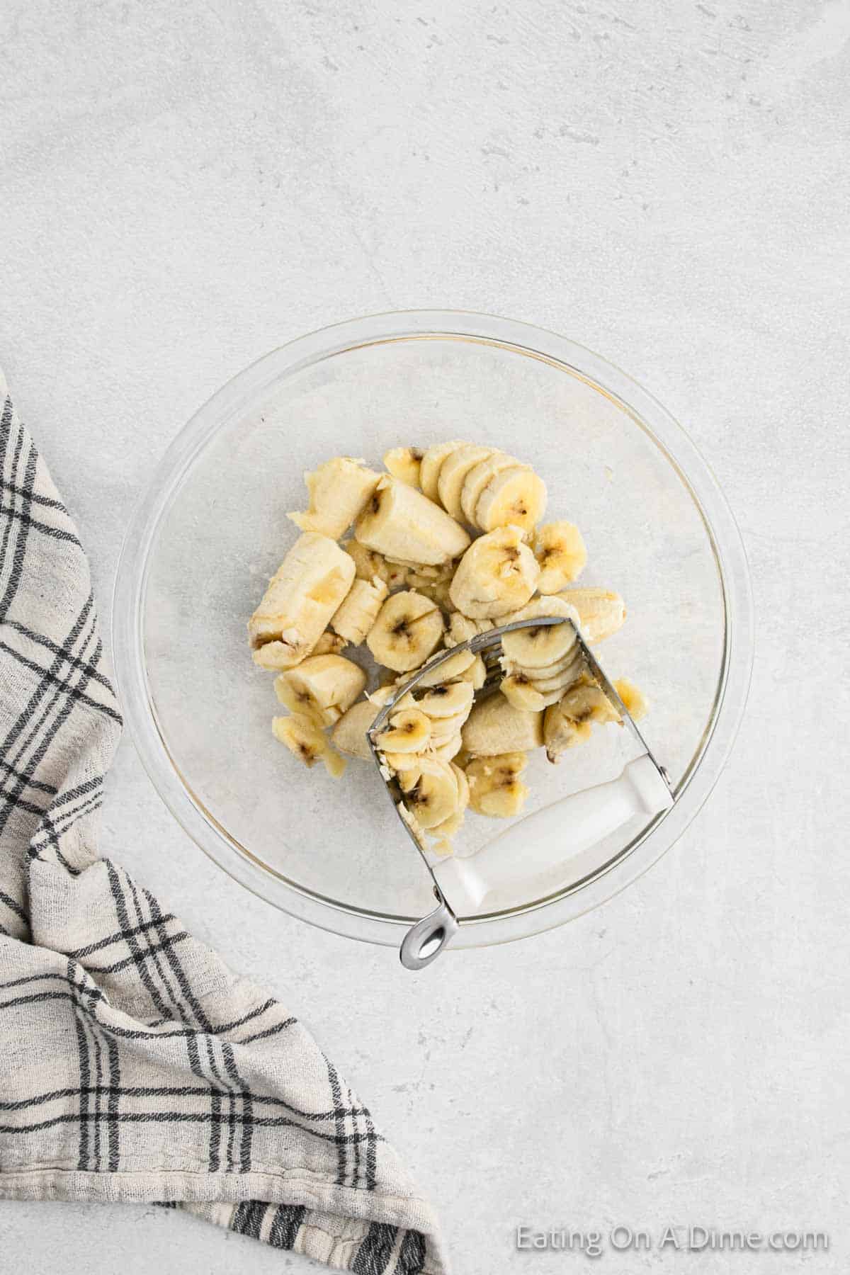 Mashing banana pieces in a bowl with a smasher