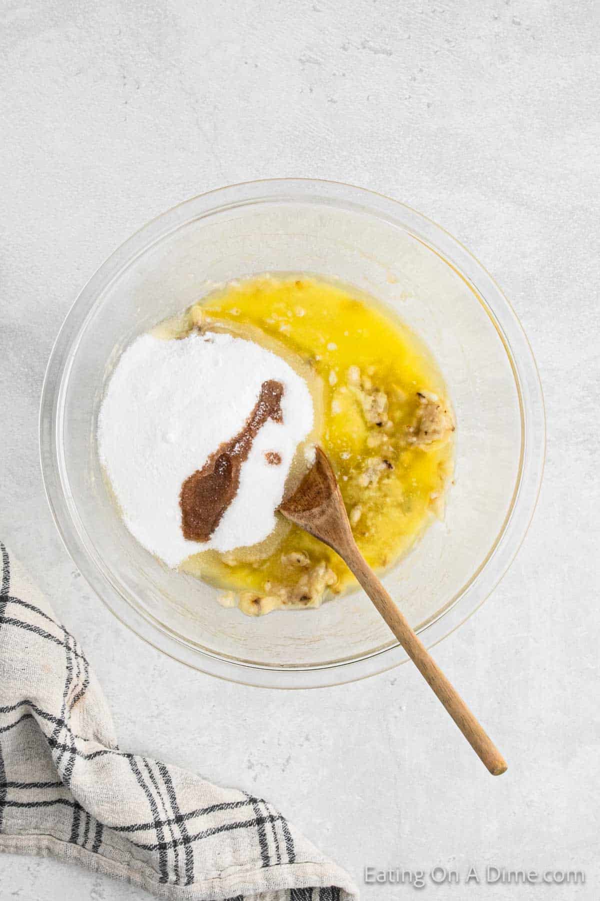 Mixing eggs, sugar, vanilla, baking soda and salt with mashed bananas with wooden spoon