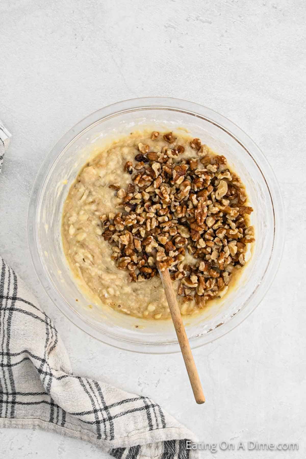 Chopped pecans mixed in banana mixture in a bowl with a wooden spoon