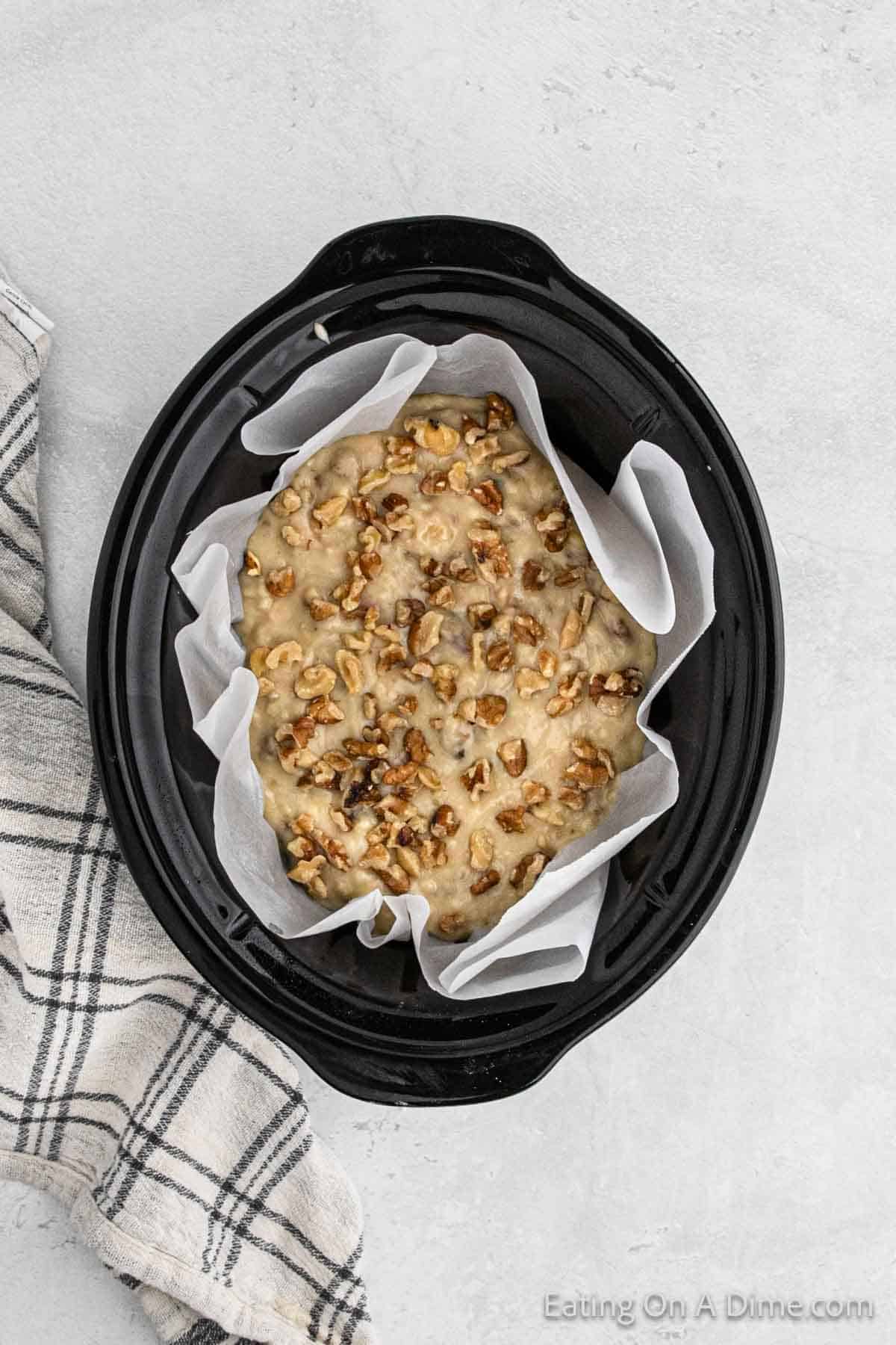 Chopped pecans on top of banana bread batter in the slow cooker