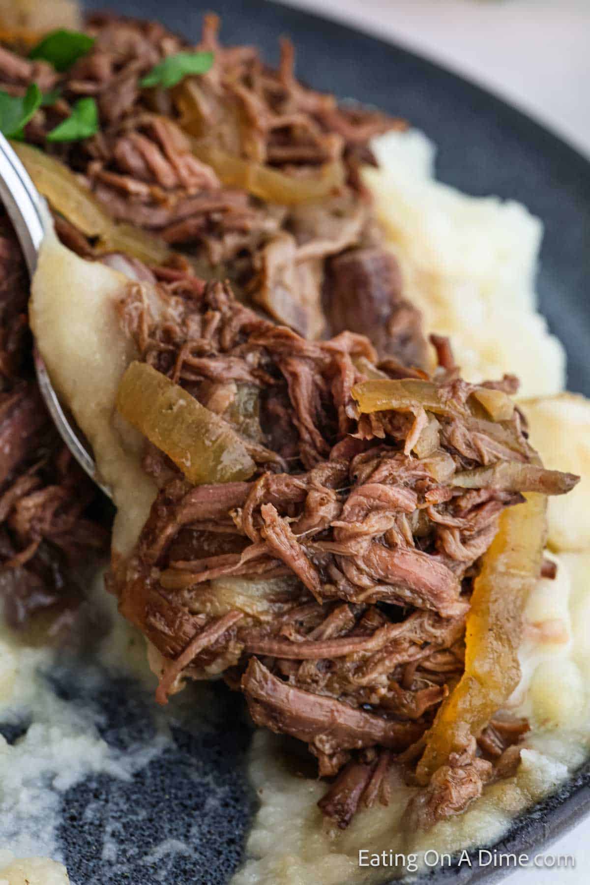 Shredded beef with cooked onions on a fork with mashed potatoes