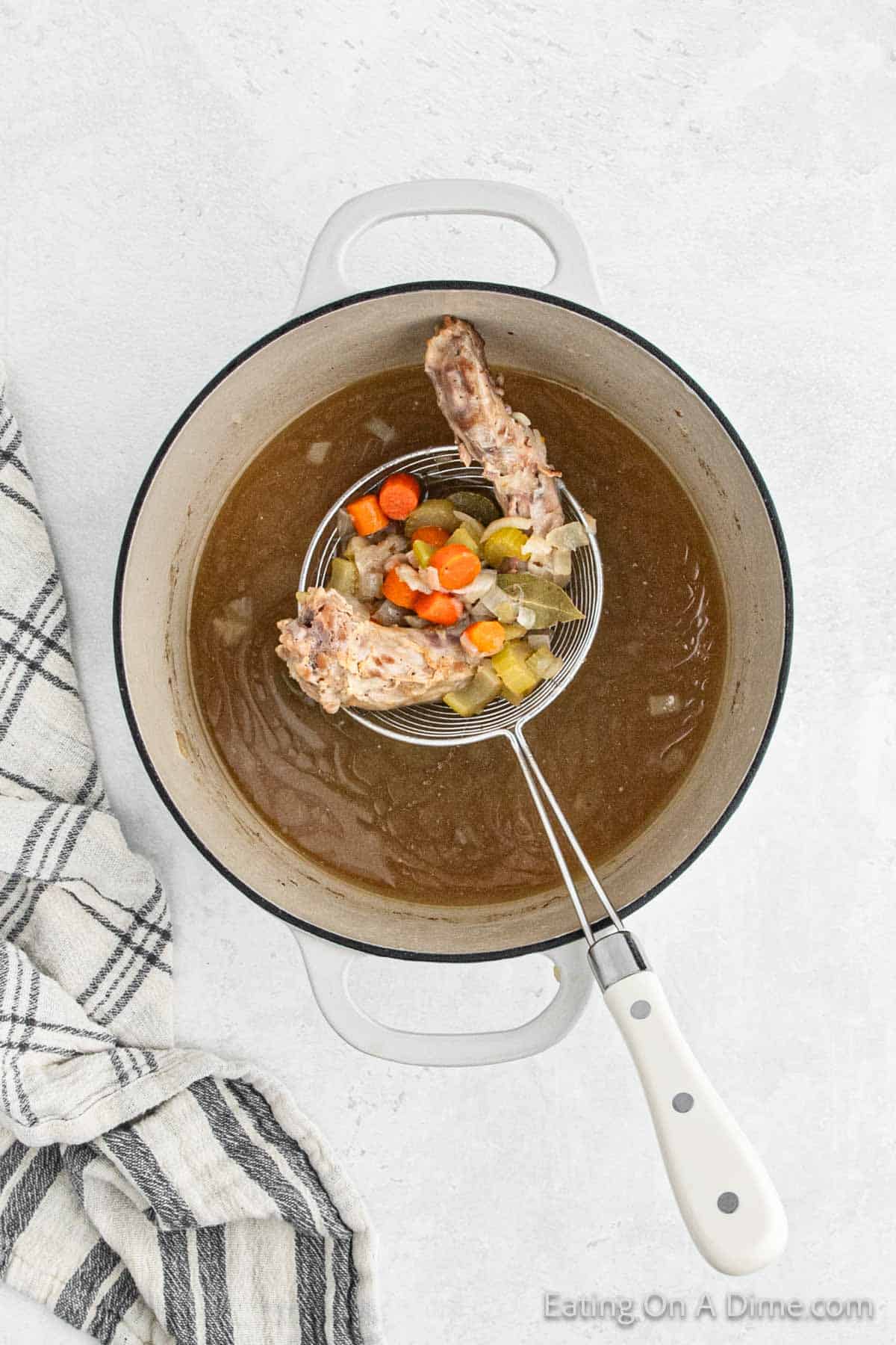 Hand held strainer over the cooked brown gravy with turkey and chopped veggies