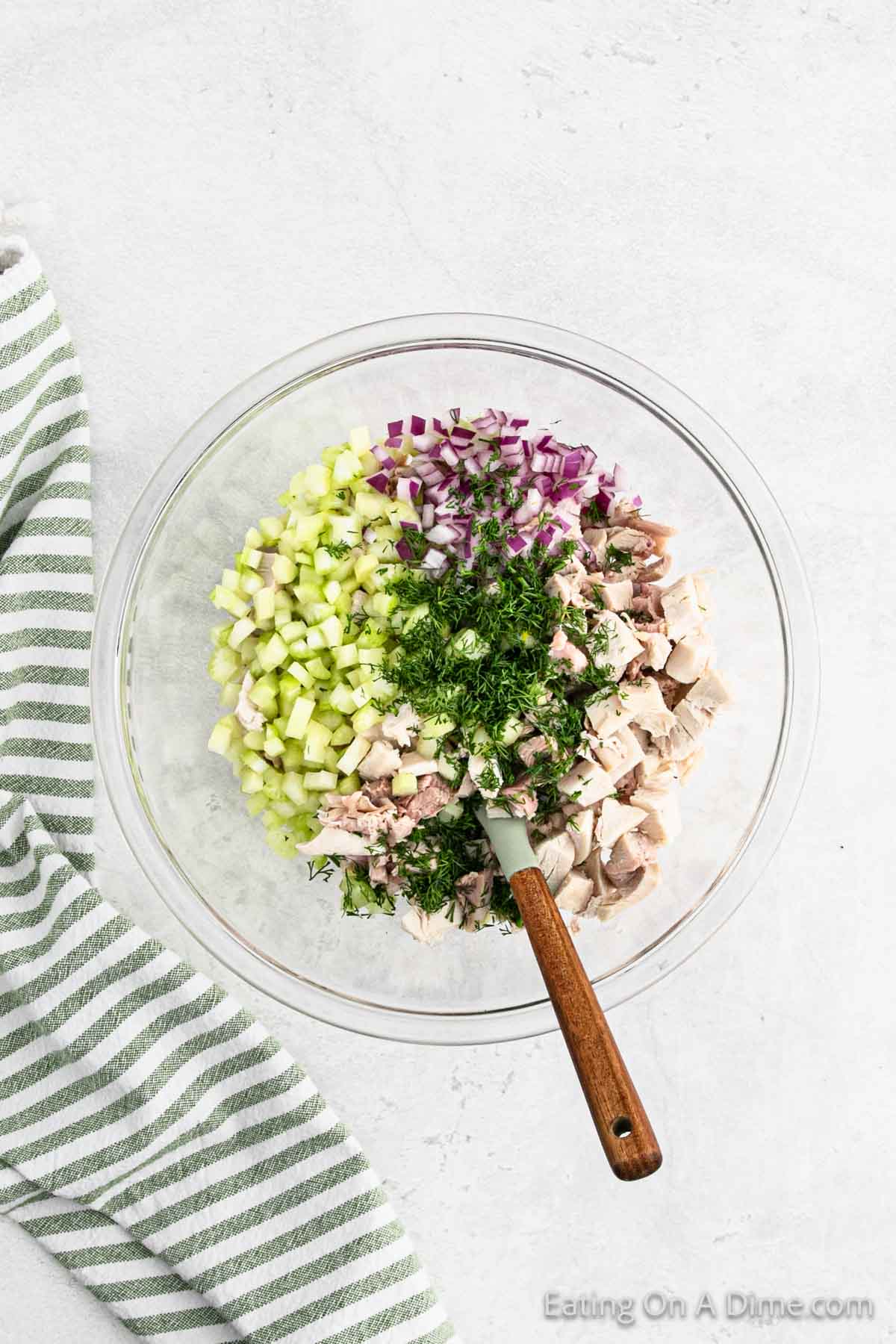 Combining turkey, celery, red onion, and fresh dill in a bowl with a spoon