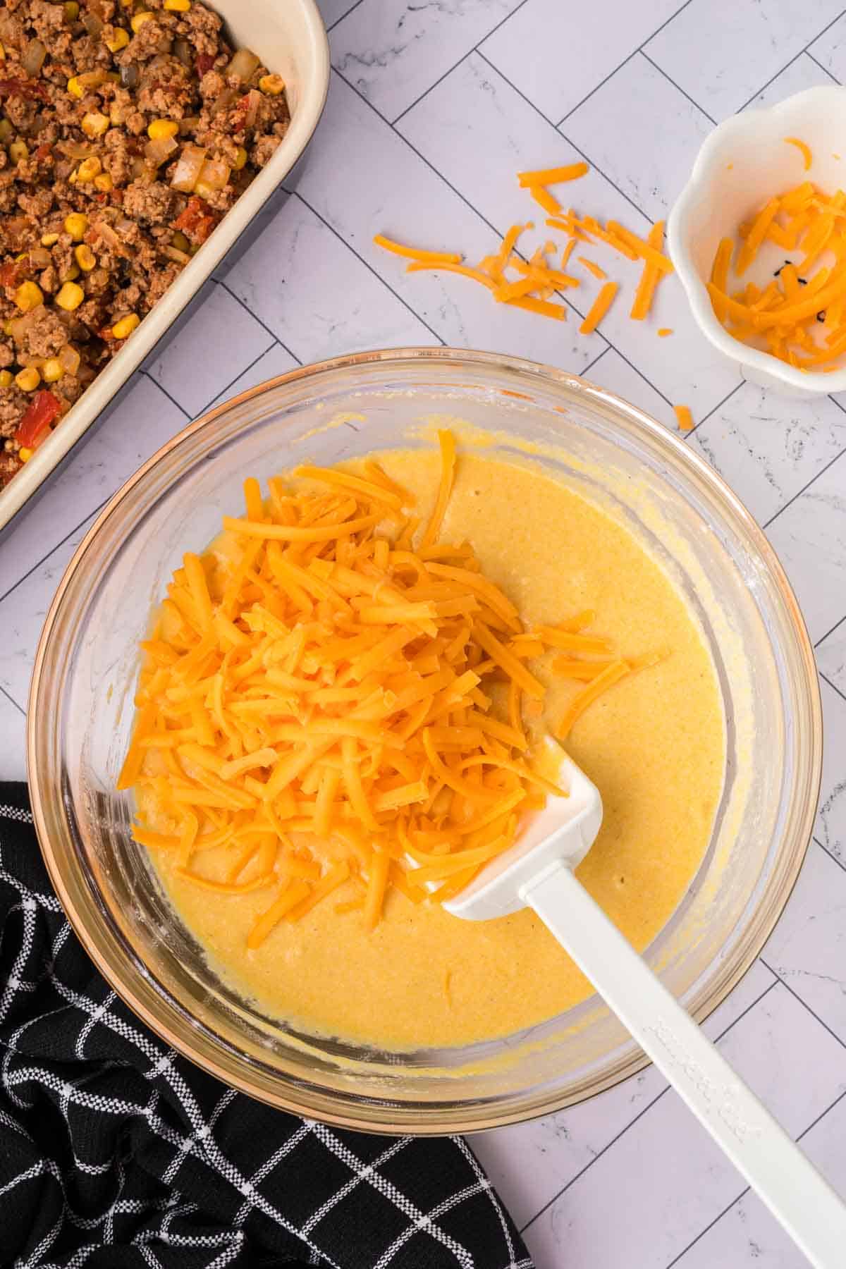 Shredded cheese mixed with the cornbread mixture in a bowl with a spatula