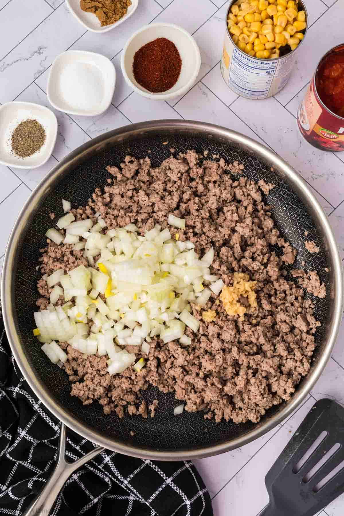 Cooked ground in a skillet topped with chopped onions