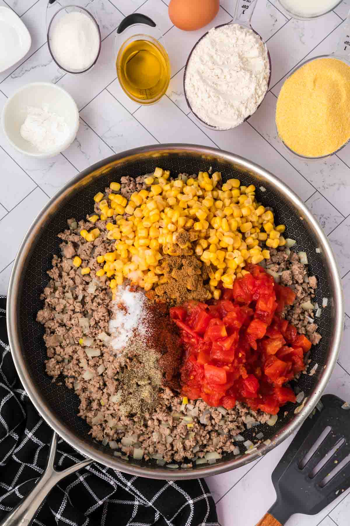 Cooked ground beef topped with corn, diced tomatoes and spices in a skillet