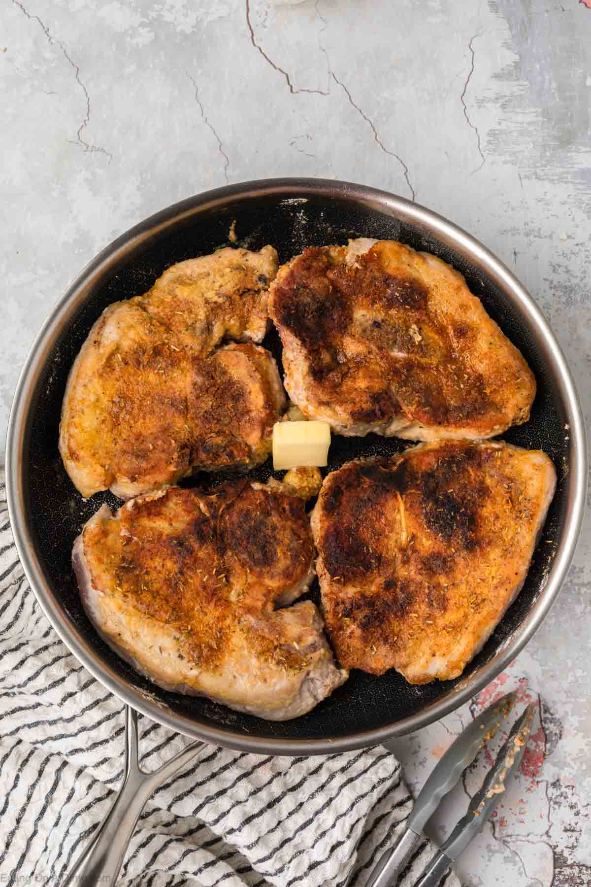 Golden brown pork chops with butter in a skillet