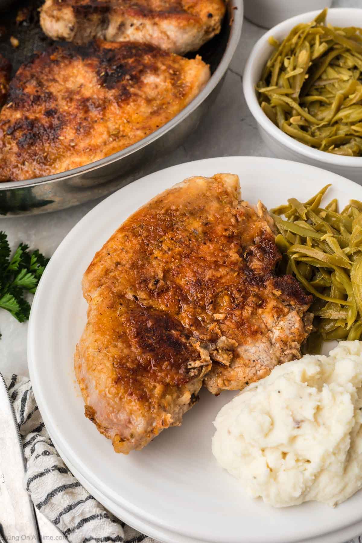 Golden Brown Pork Chops on a plate with a side of French Style Green Beans with mashed potatoes