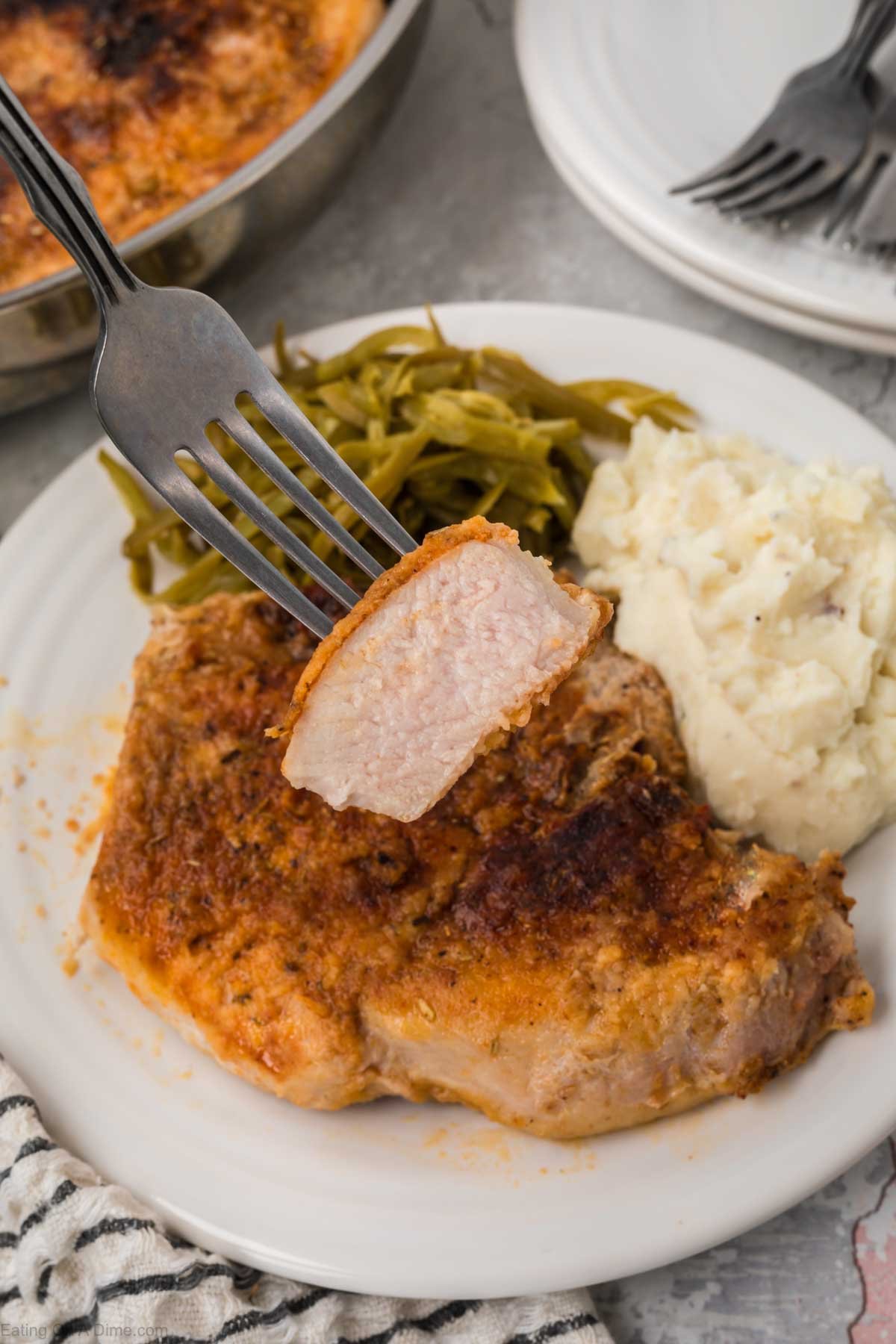 Golden brown pork chops on a plate with a side of green beans and mashed potatoes 