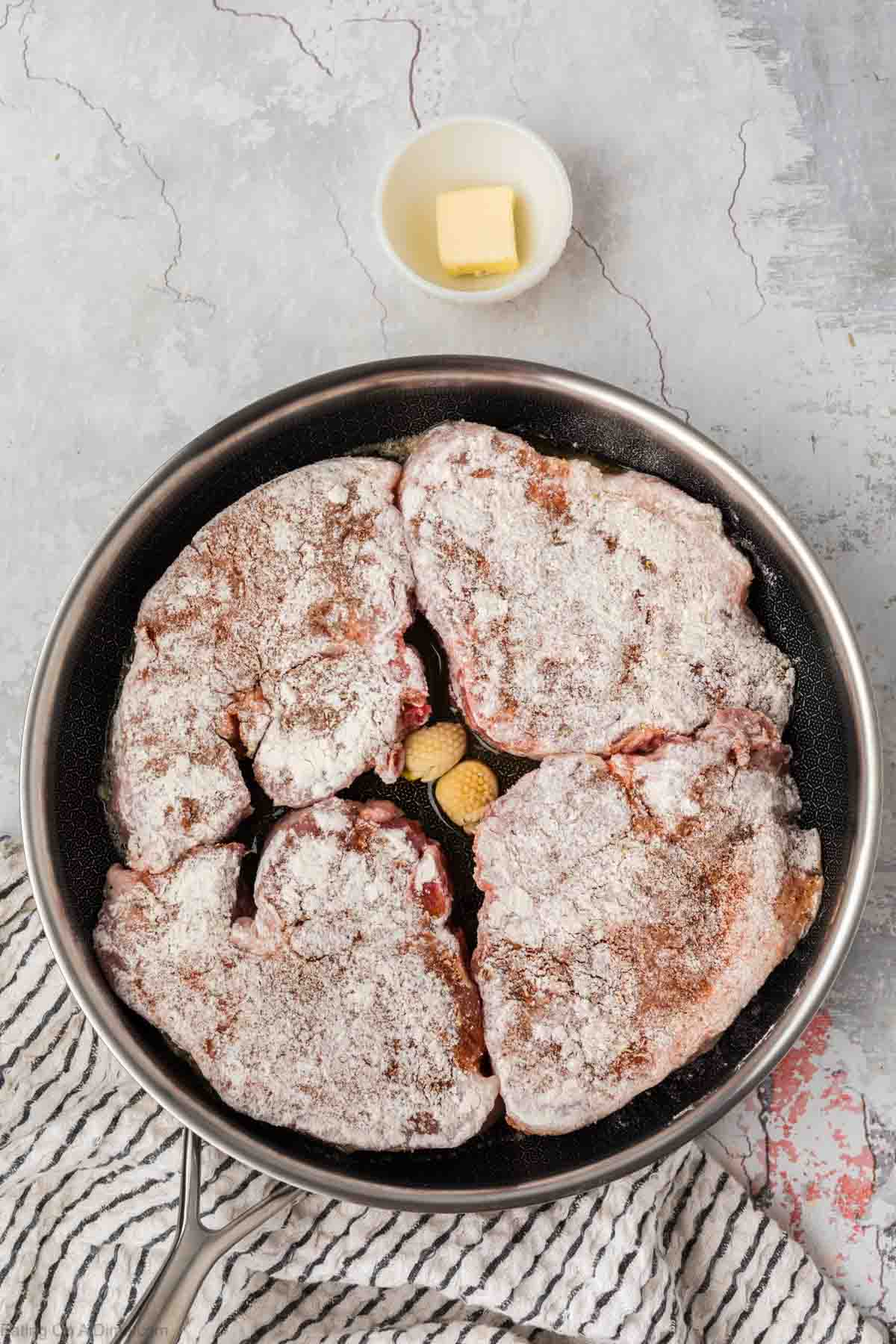 Flour pork chops placed in the skillet with garlic cloves