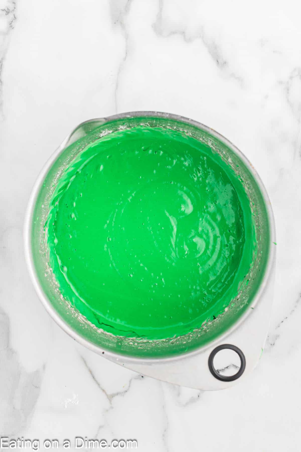 A bowl filled with vibrant green cake batter sits on a white marble surface, reminiscent of festive Christmas colors.