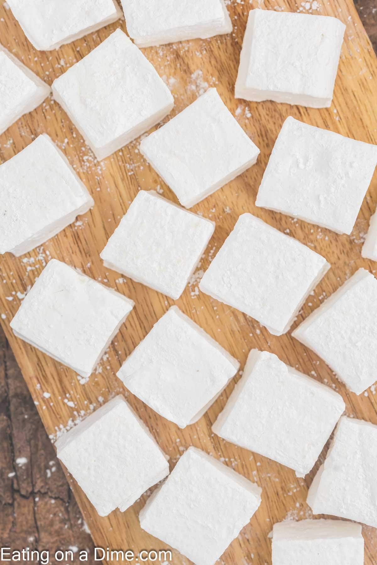 Homemade squares of white marshmallows dusted with powdered sugar are artfully arranged on a rustic wooden surface.