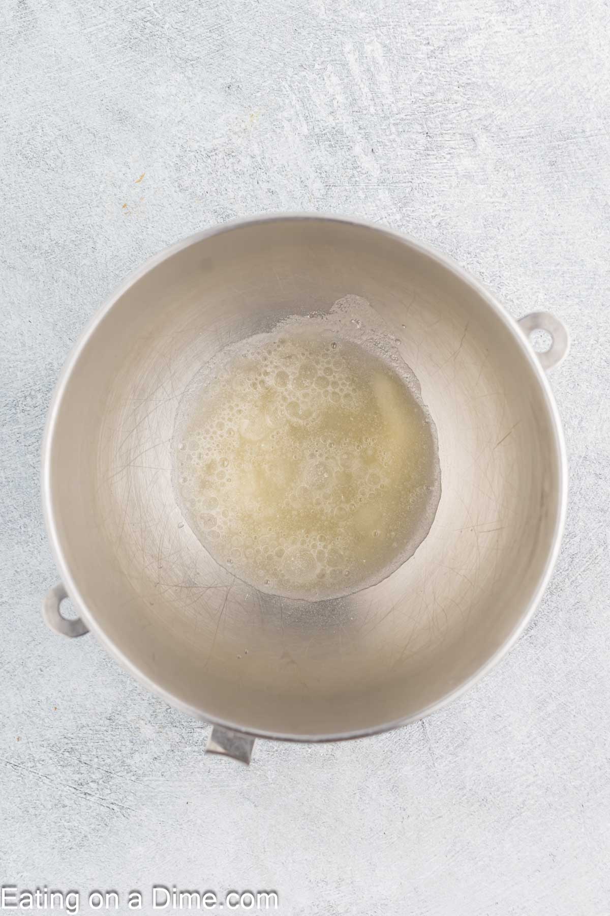 A metal mixing bowl on a light gray countertop contains foamy egg whites, the first step toward crafting homemade marshmallows.